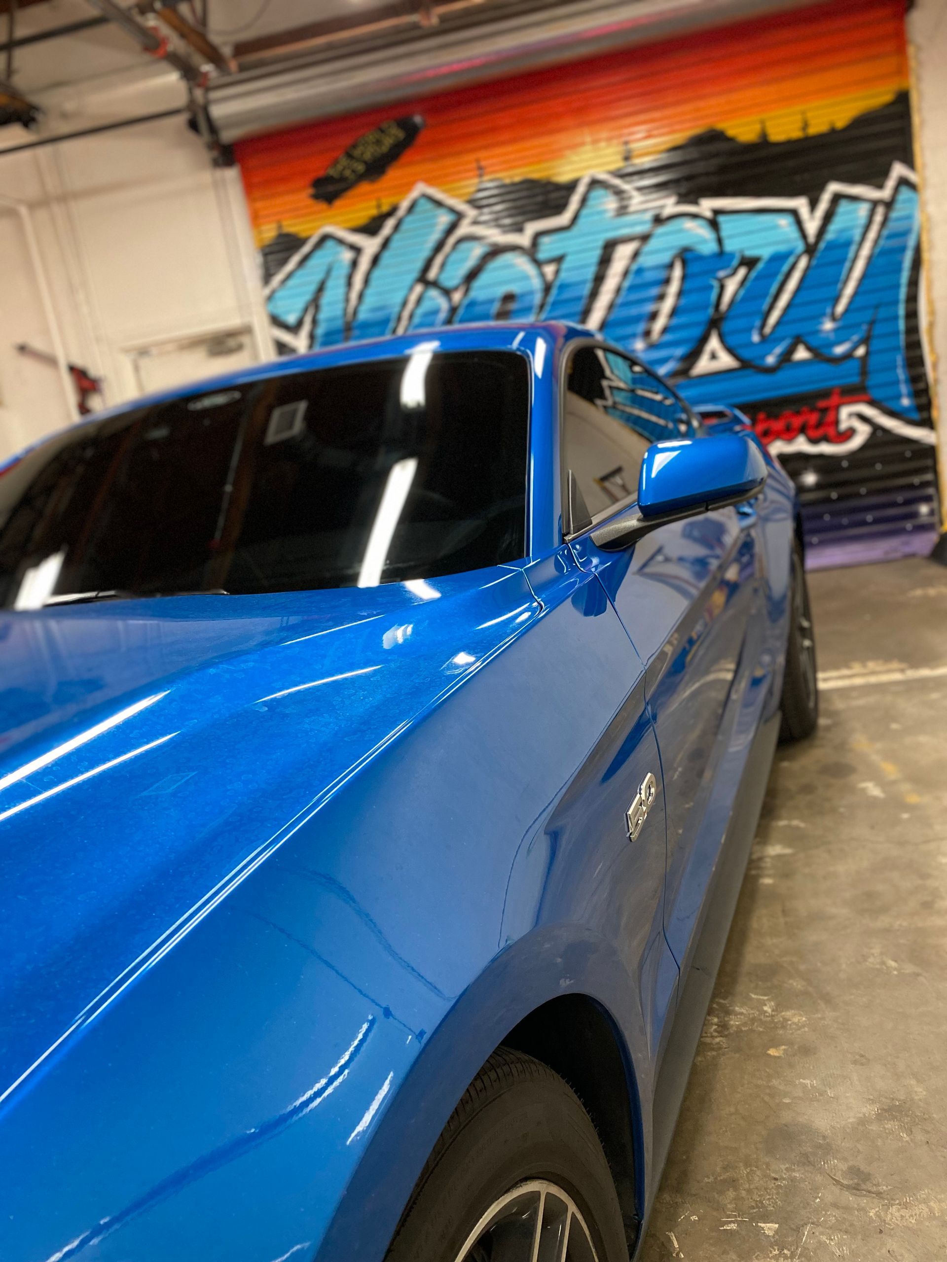 Blue sports car inside a garage with a colorful mural in the background