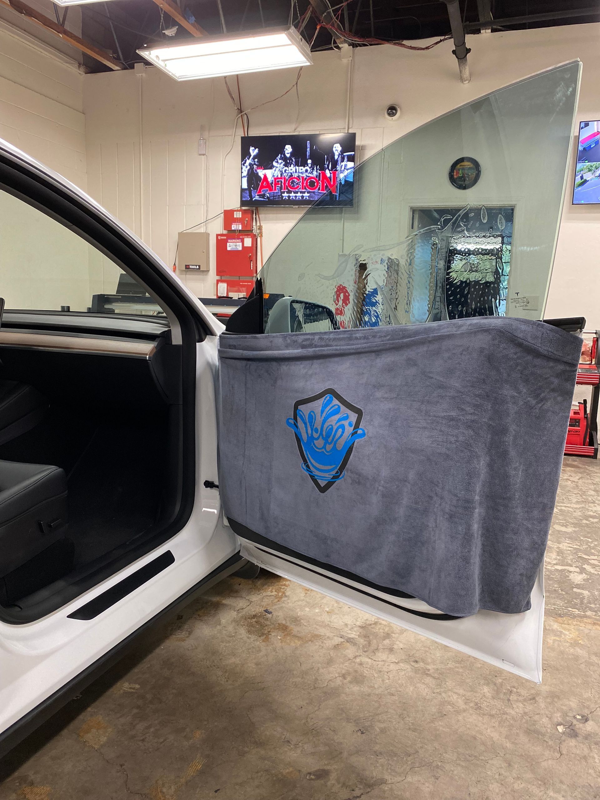 Gray protective car door cover on open white vehicle door inside an auto shop.