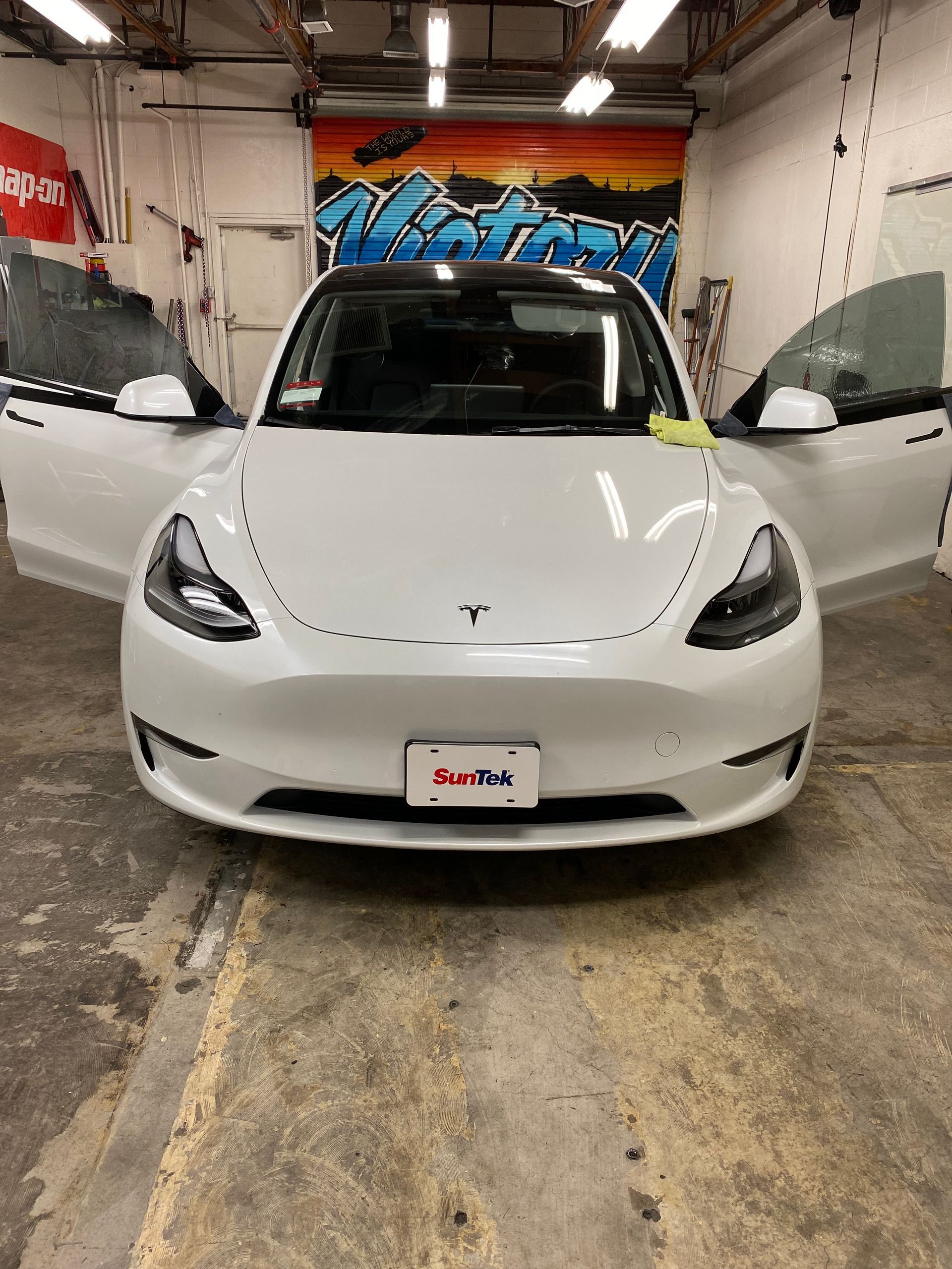White Tesla sedan in a garage with both front doors open, facing forward.