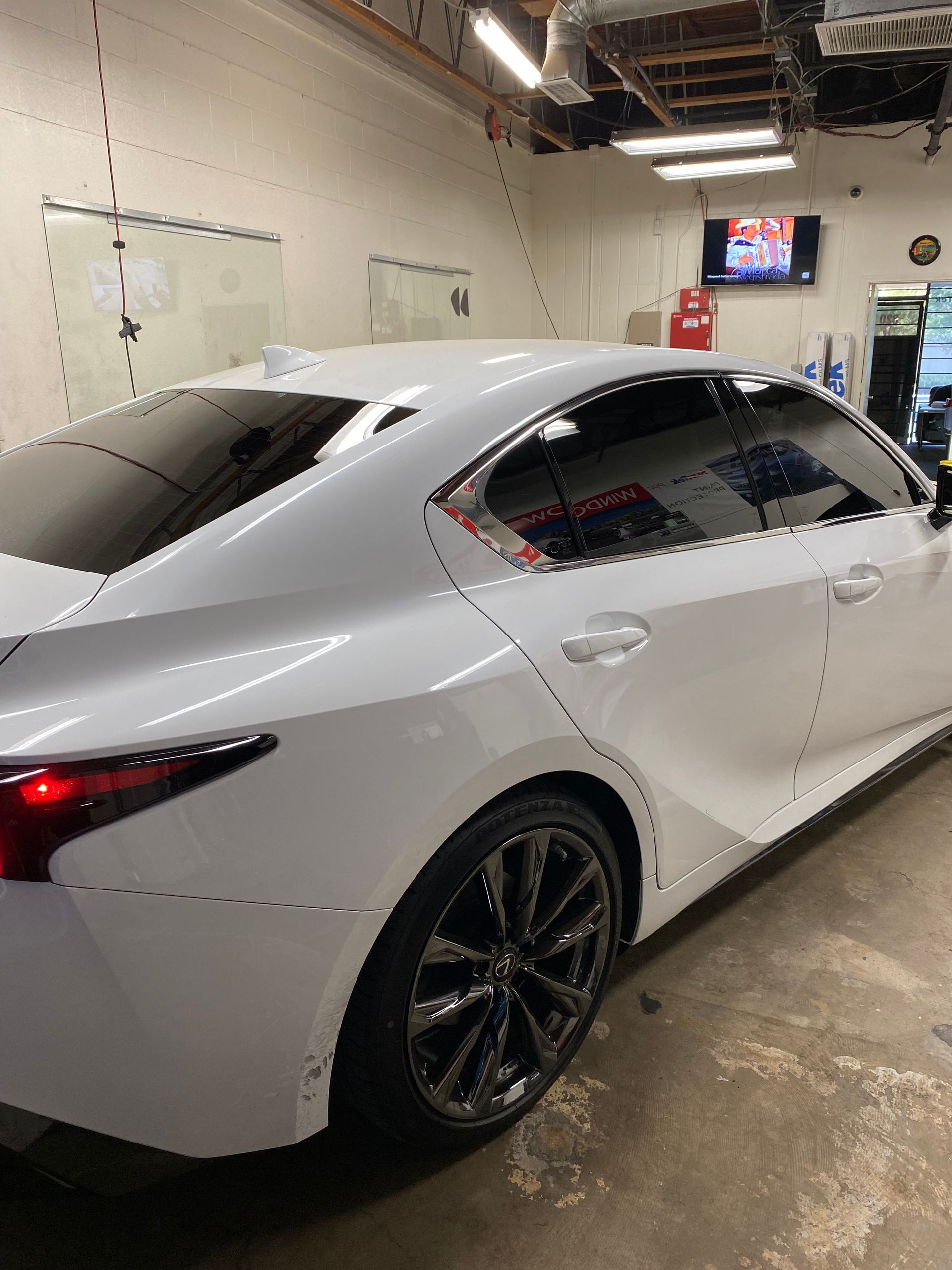 White sedan parked in a garage, side view with black wheels and tinted windows.