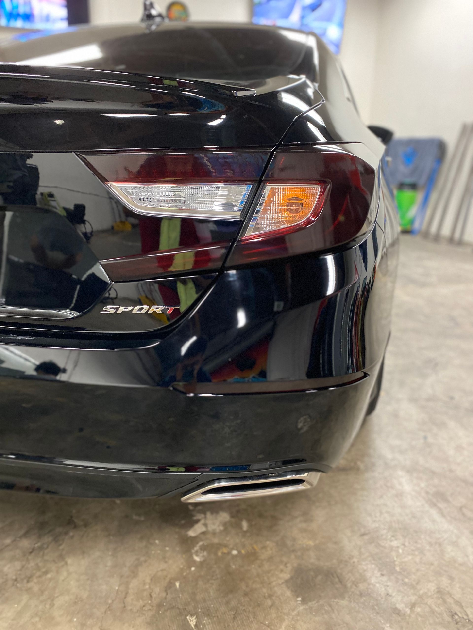 Black sedan rear bumper with a visible dent and scratches in a garage or repair shop