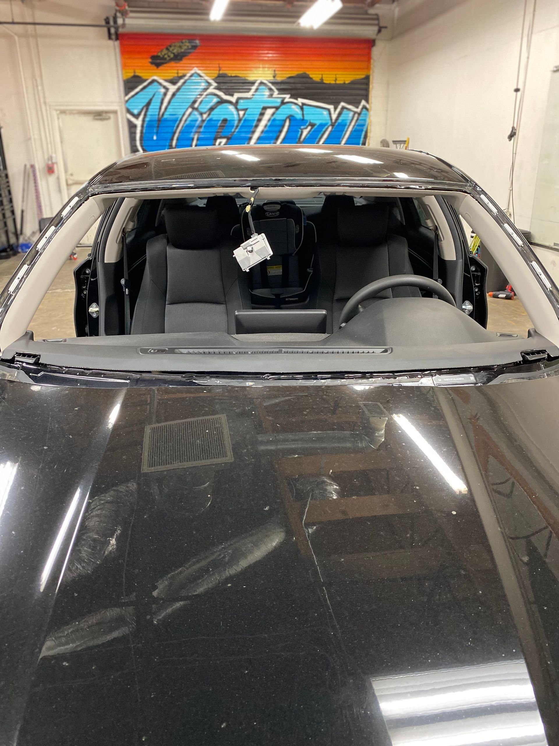 Dusty black car in a garage, viewed through the windshield with a damaged, missing roof.