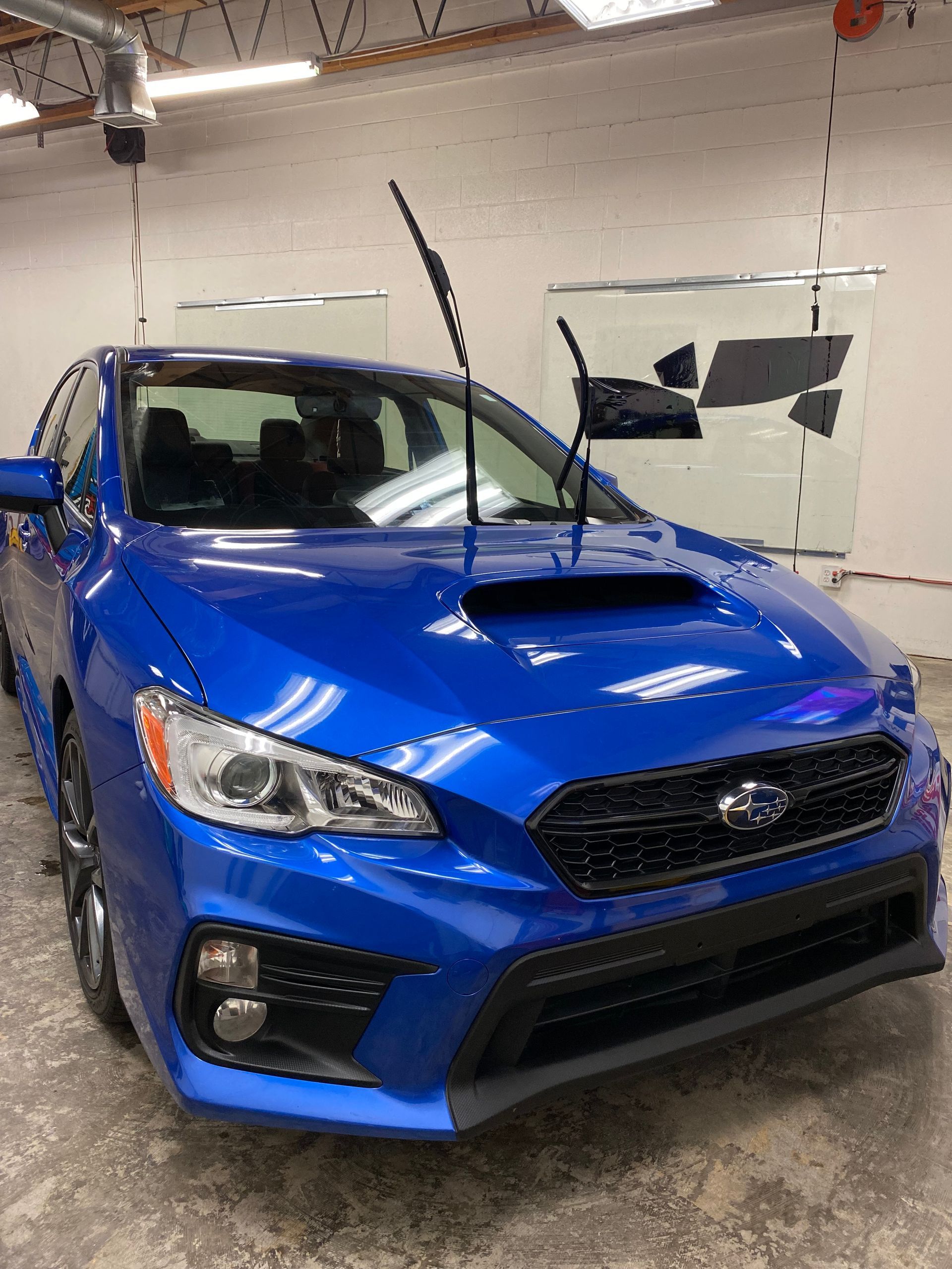 Blue sports sedan in an indoor garage with windshield wipers raised.