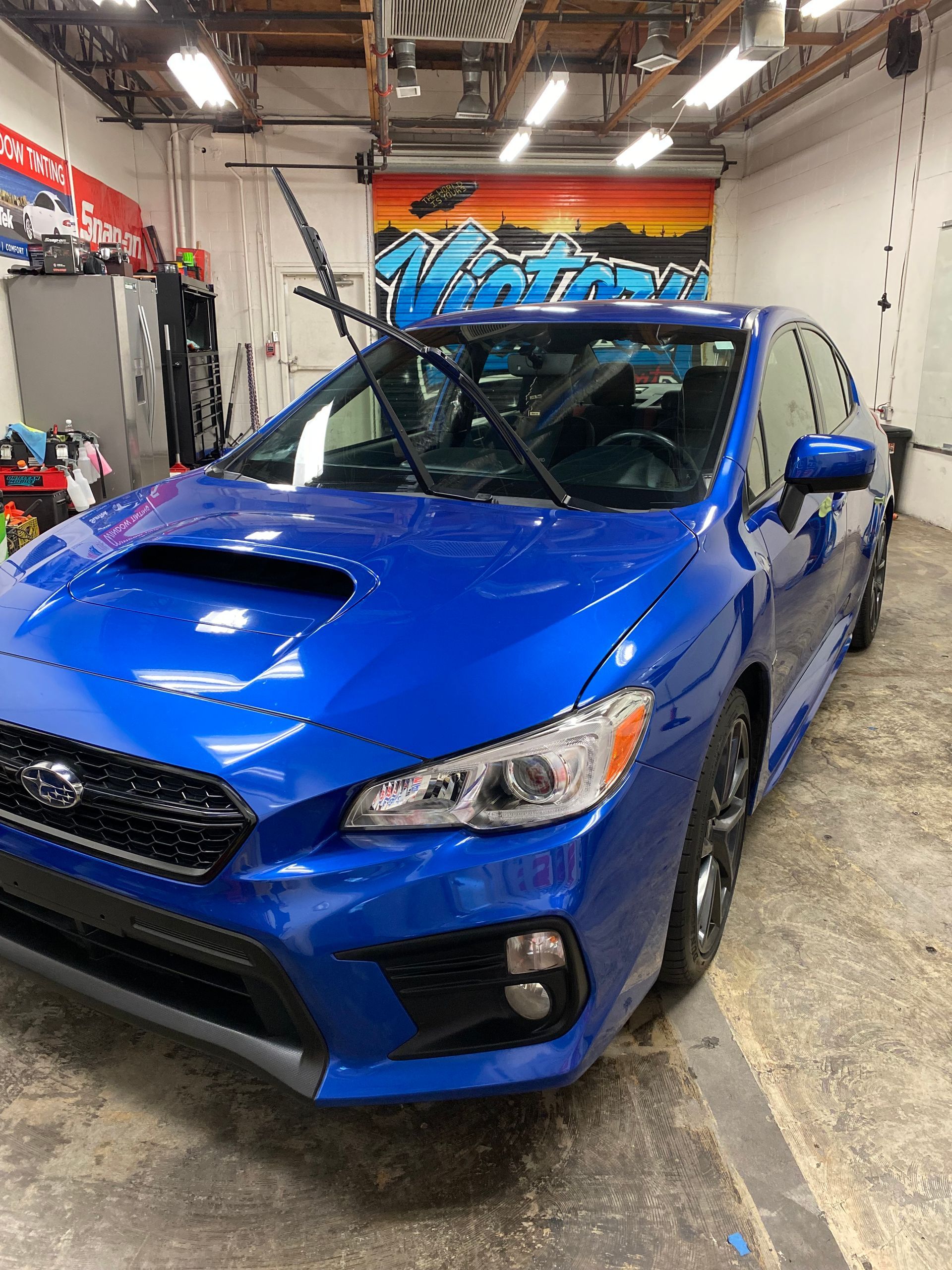 Blue Subaru hatchback in a garage with its hood scoop visible.
