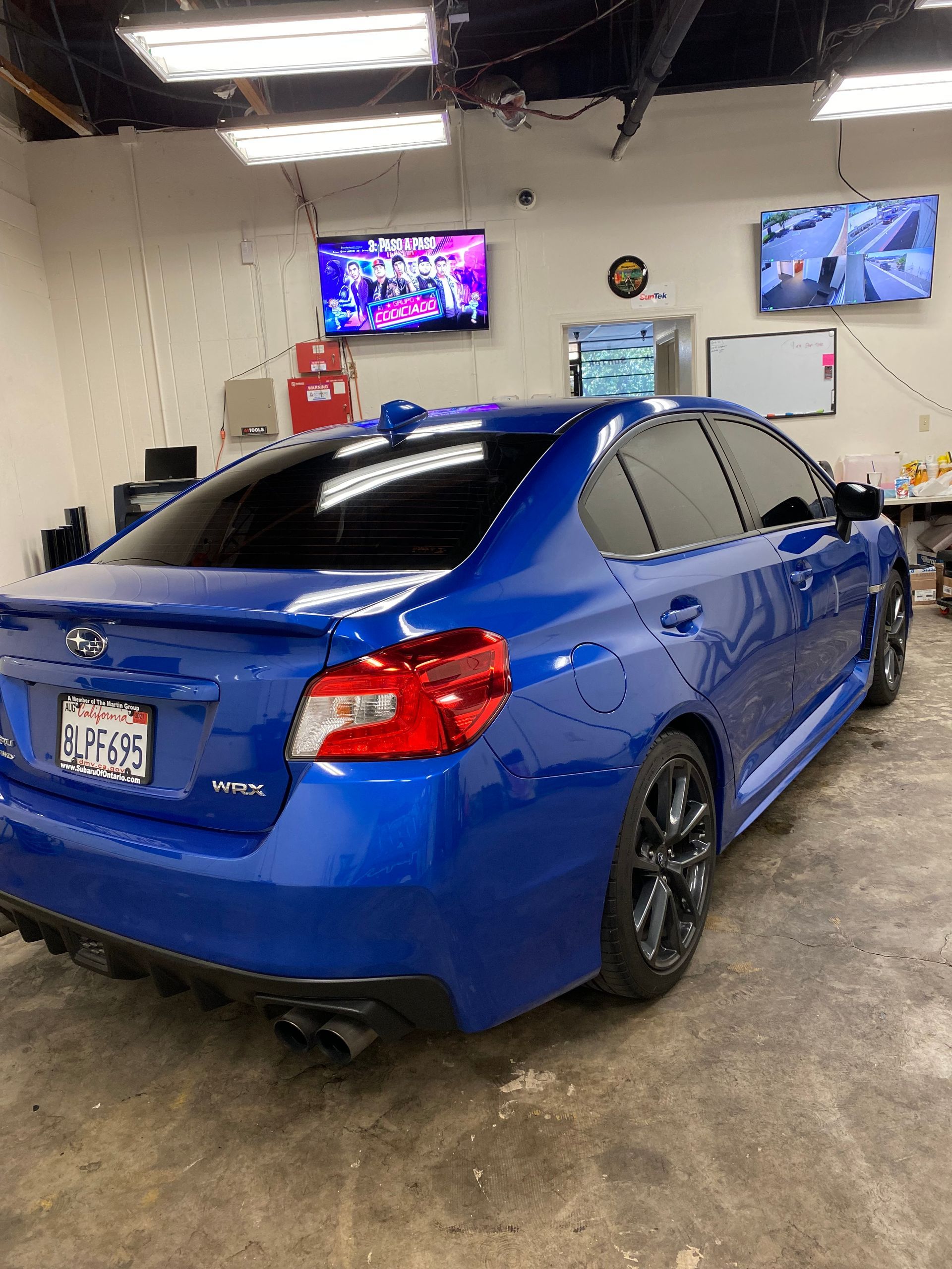 Blue sedan in a car detailing bay with TV screens on the wall.