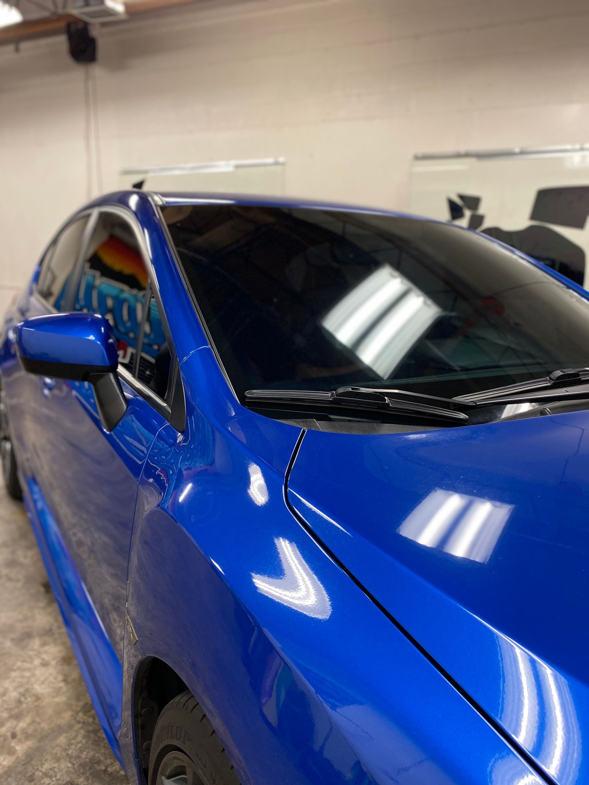 Blue car parked indoors under bright ceiling lights, seen from the front-left side.