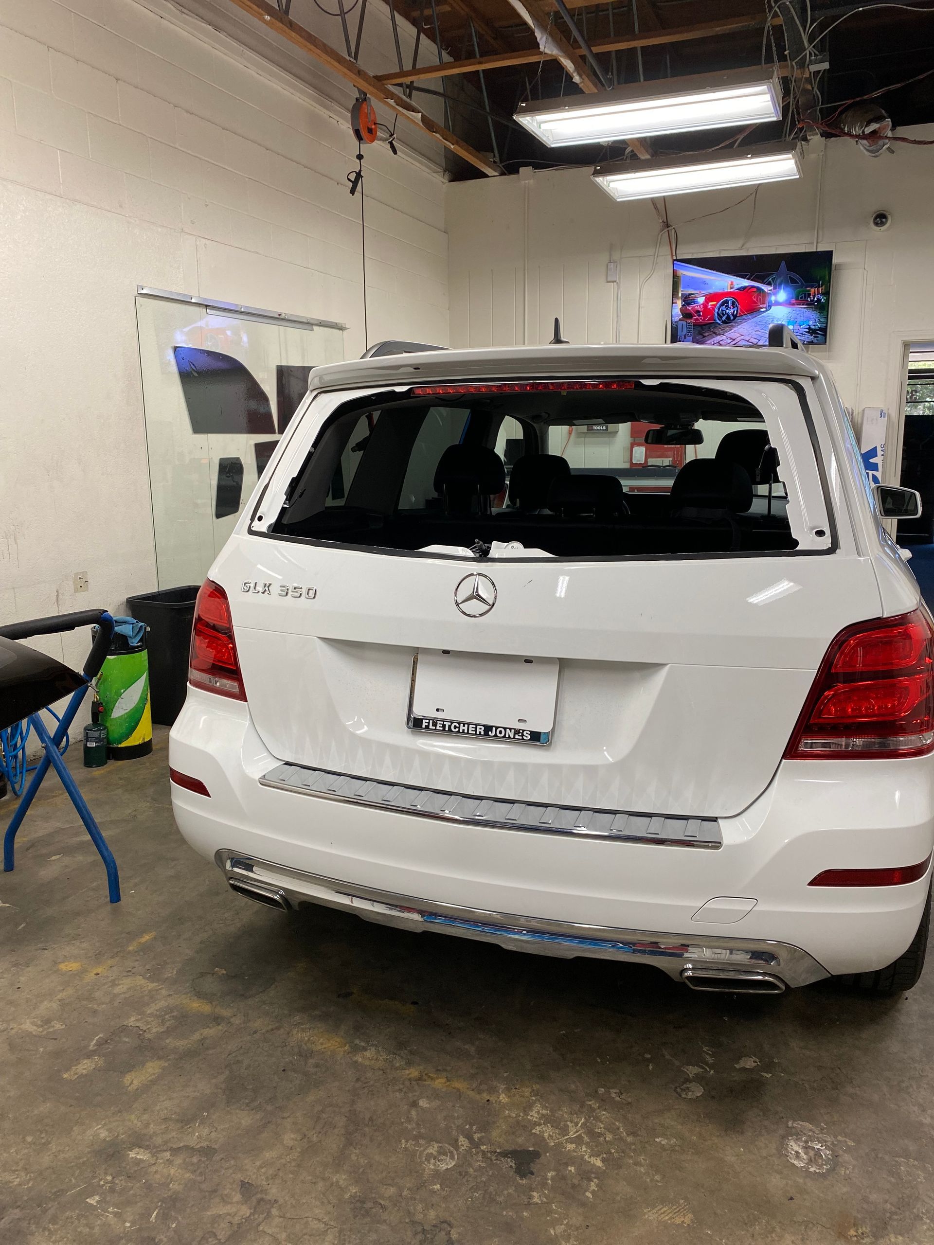 White Mercedes SUV parked inside a garage, rear view with wet floor and fluorescent lights.