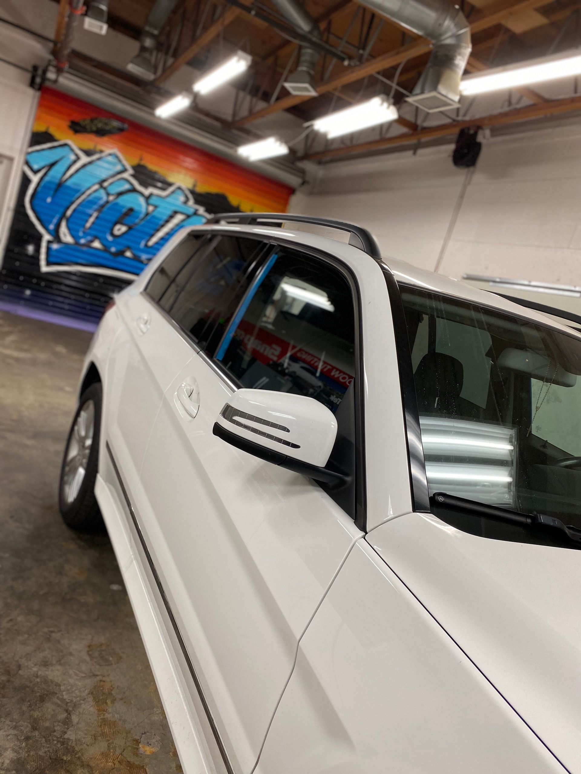 White SUV indoors in a garage, with a blue mural on the wall and overhead lights visible