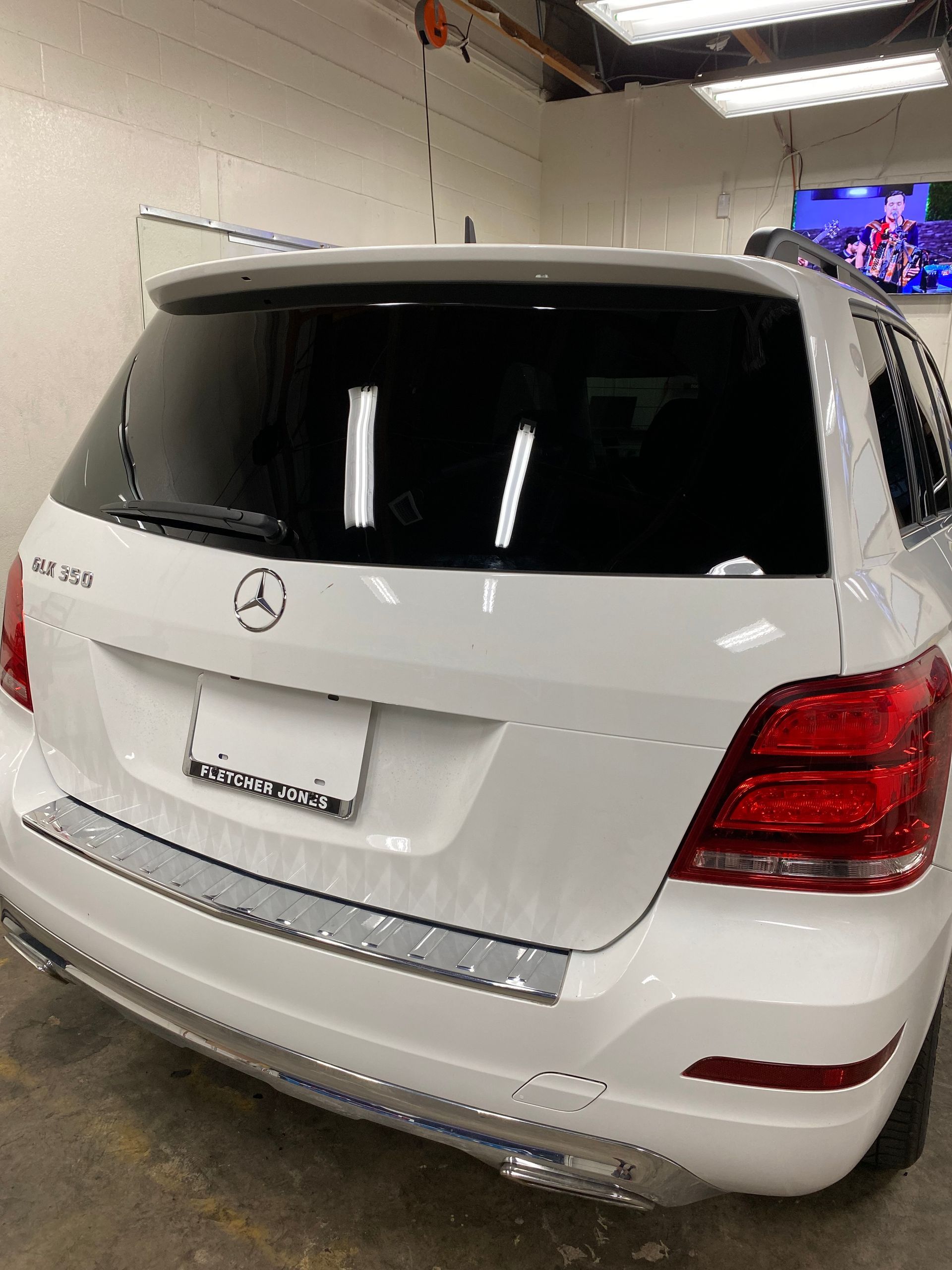 White Mercedes-Benz SUV parked indoors in a garage, rear view with tinted windows.