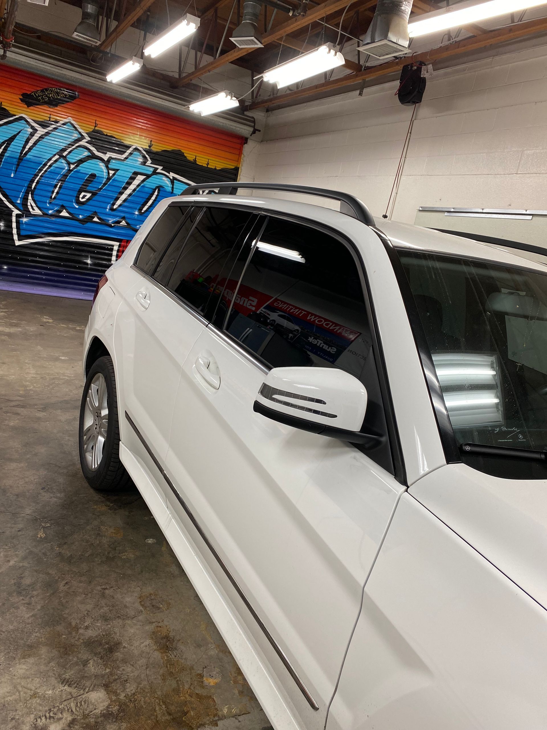 White SUV parked indoors beside a colorful mural in a garage or showroom