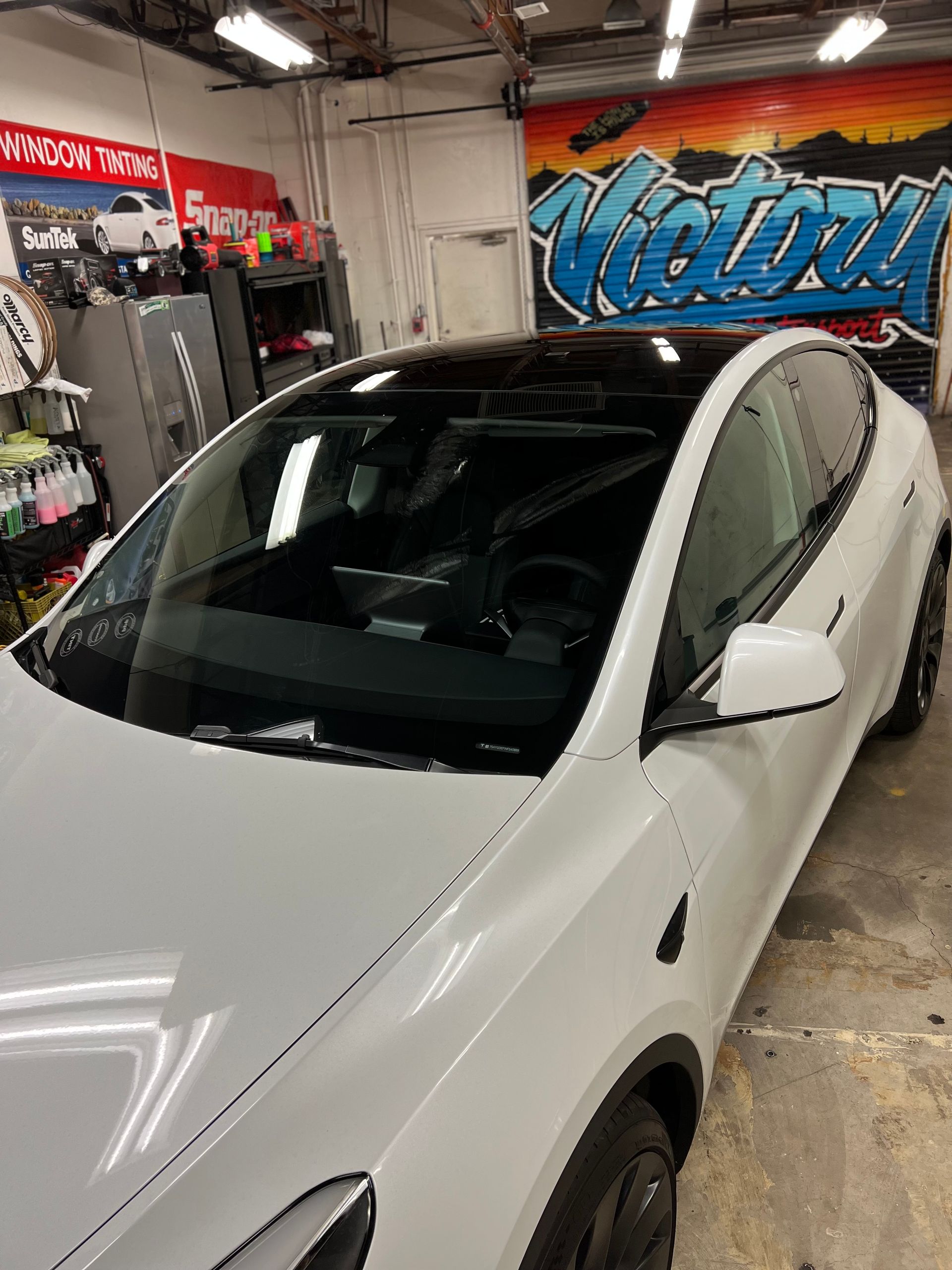 White Tesla in a detailing shop with colorful wall art.