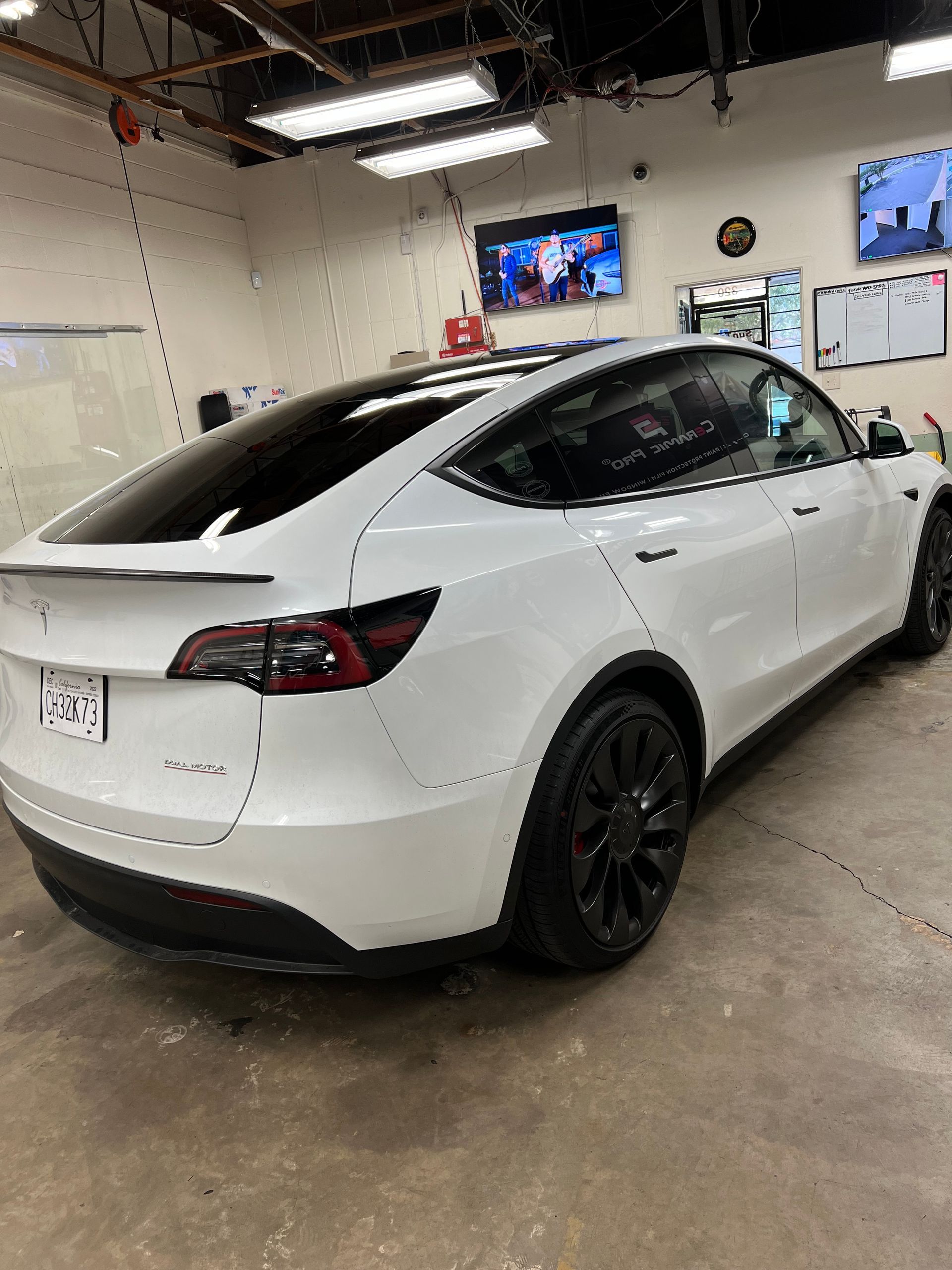 White Tesla SUV in a service bay, rear three-quarter view, with black wheels and a liftgate spoiler.