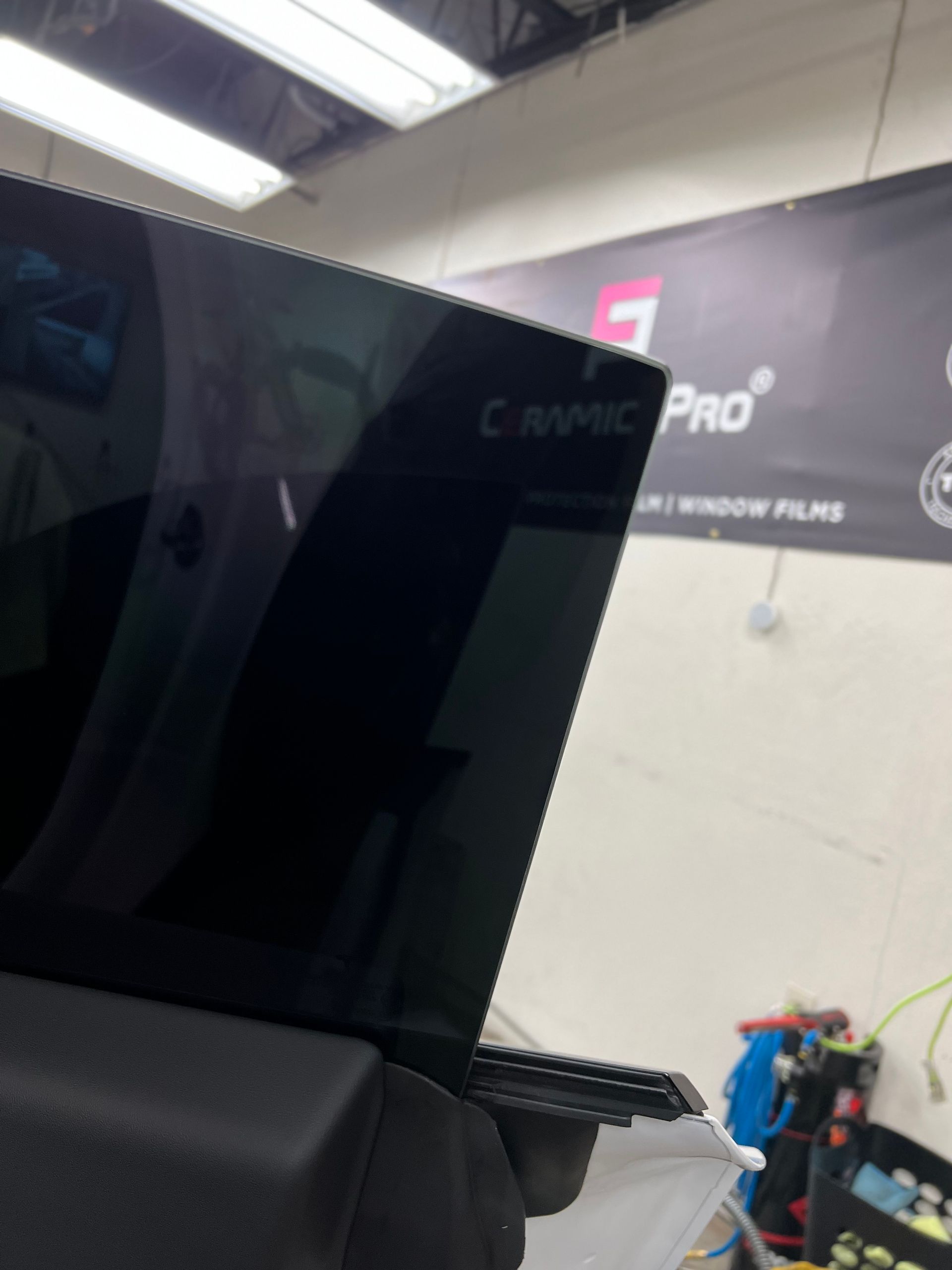 Tinted car window being installed in a workshop under bright overhead lights.