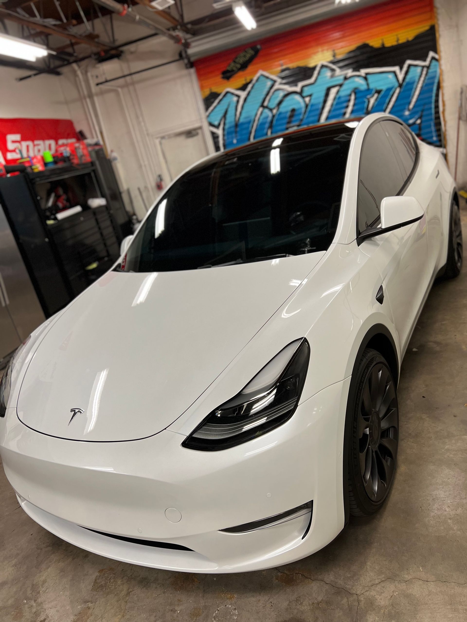 White Tesla in a garage with a colorful wall mural behind it