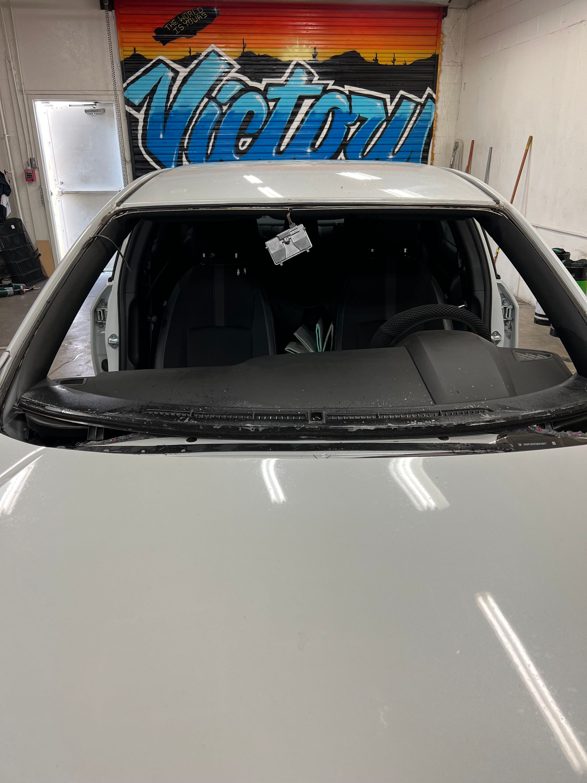 White car in a garage, viewed from the front, with a colorful “Victory” mural behind it.