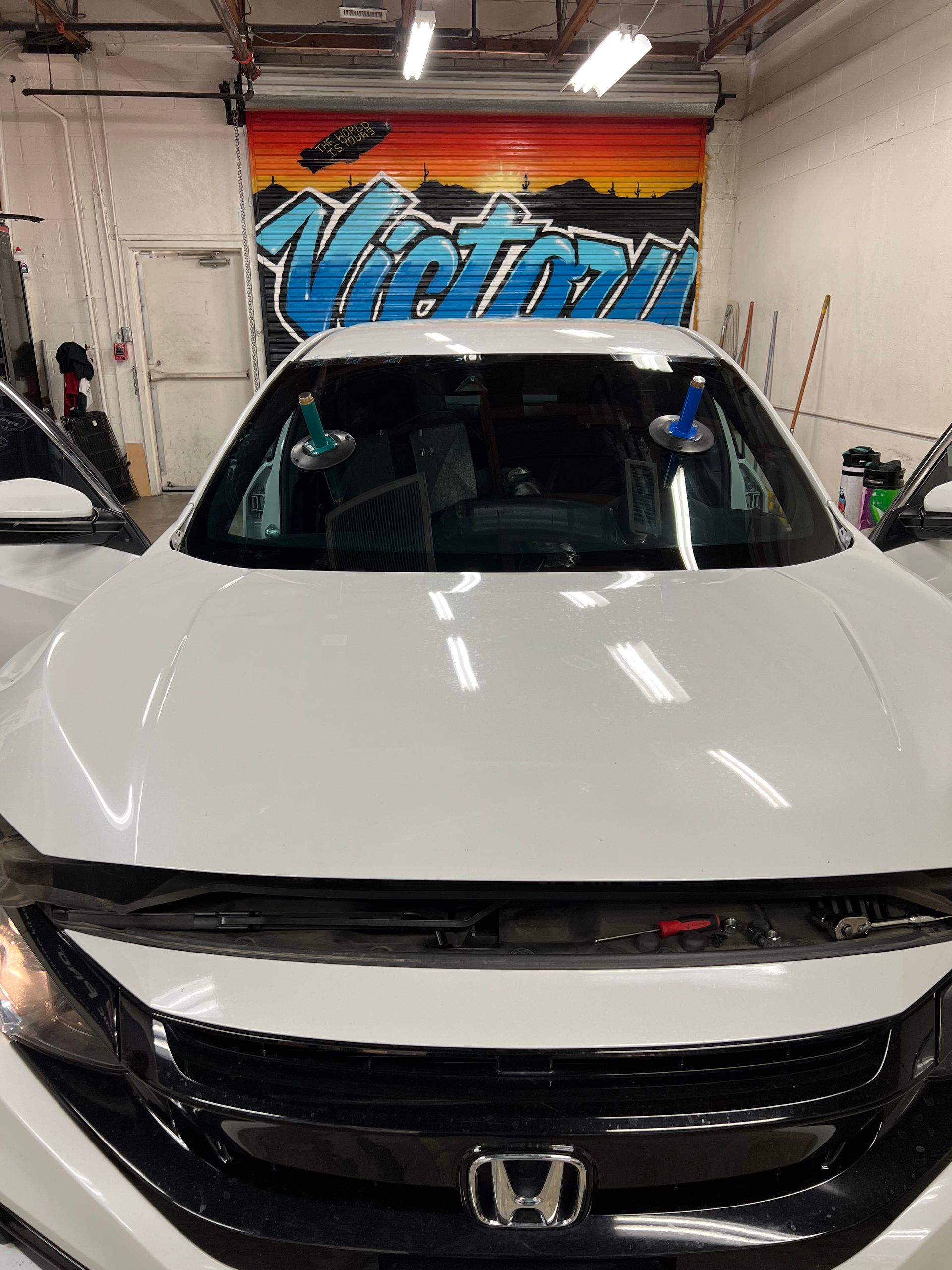 White Honda in a garage with a colorful graffiti mural behind it.
