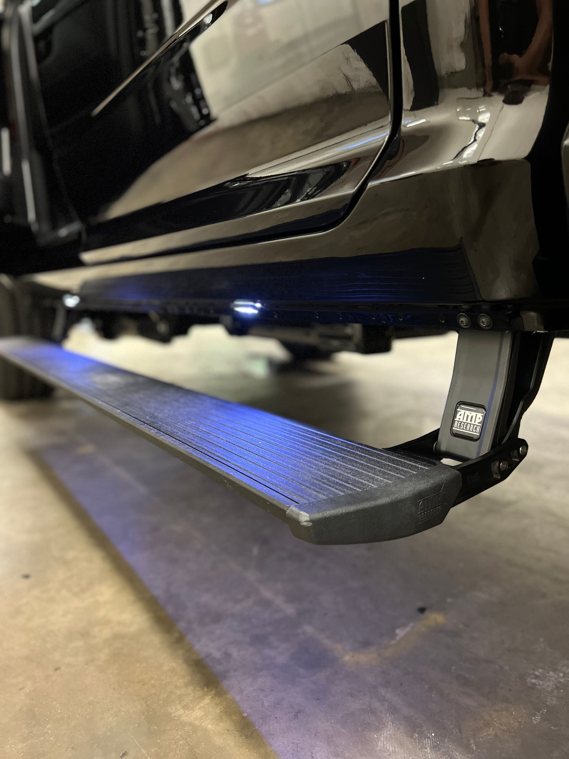 Black truck with illuminated blue running board steps parked on concrete floor