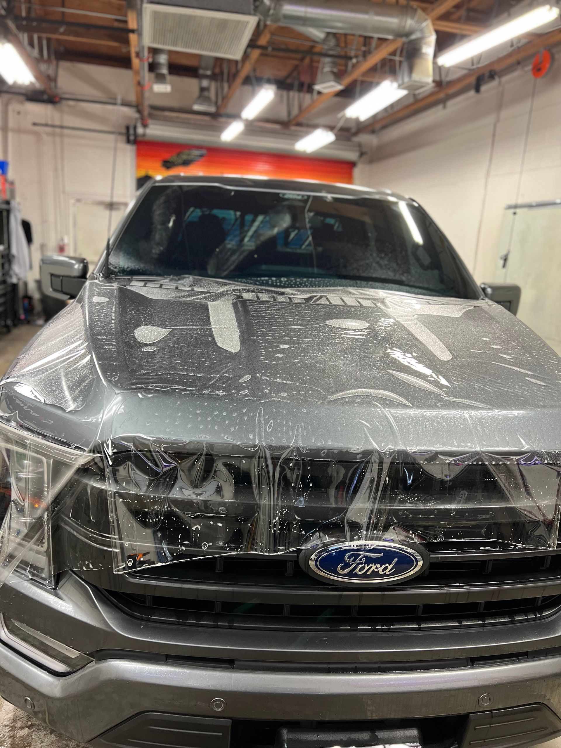 Silver Ford truck covered in soap foam inside an auto detailing bay