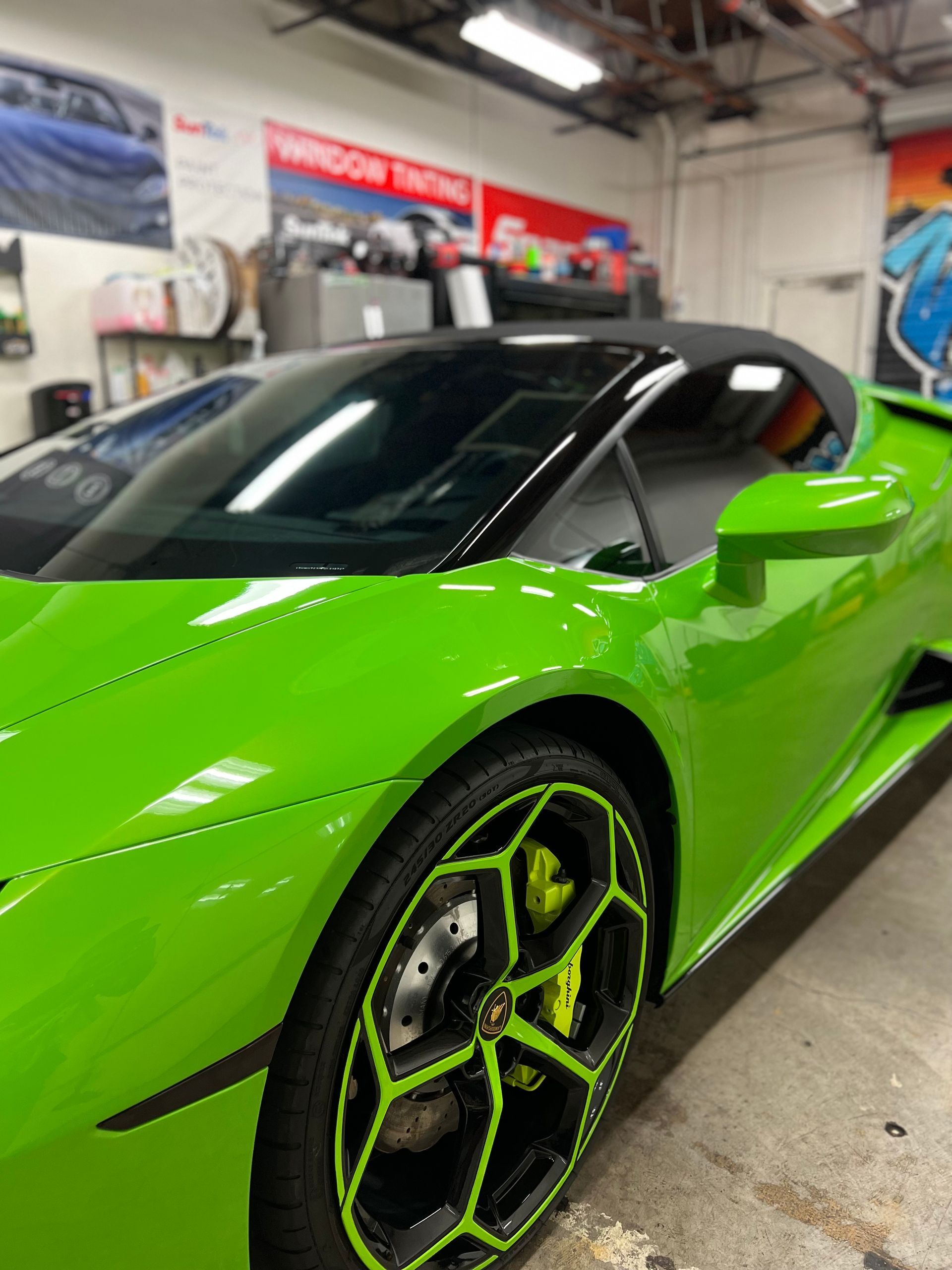 Bright green sports car with black roof and neon-accented wheels in an indoor garage