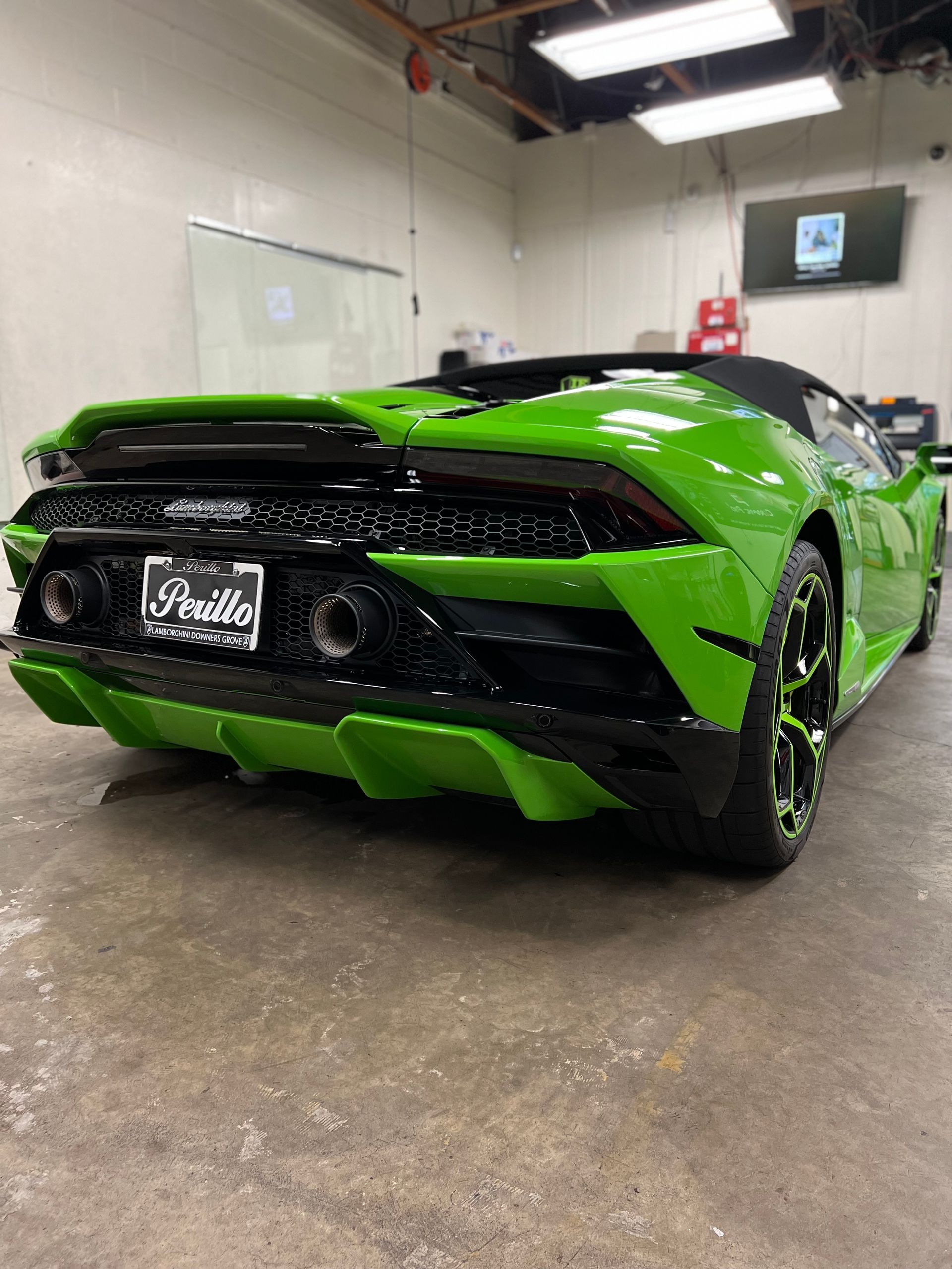 Bright green sports car viewed from the rear in an indoor garage, with black accents and wet floor reflections