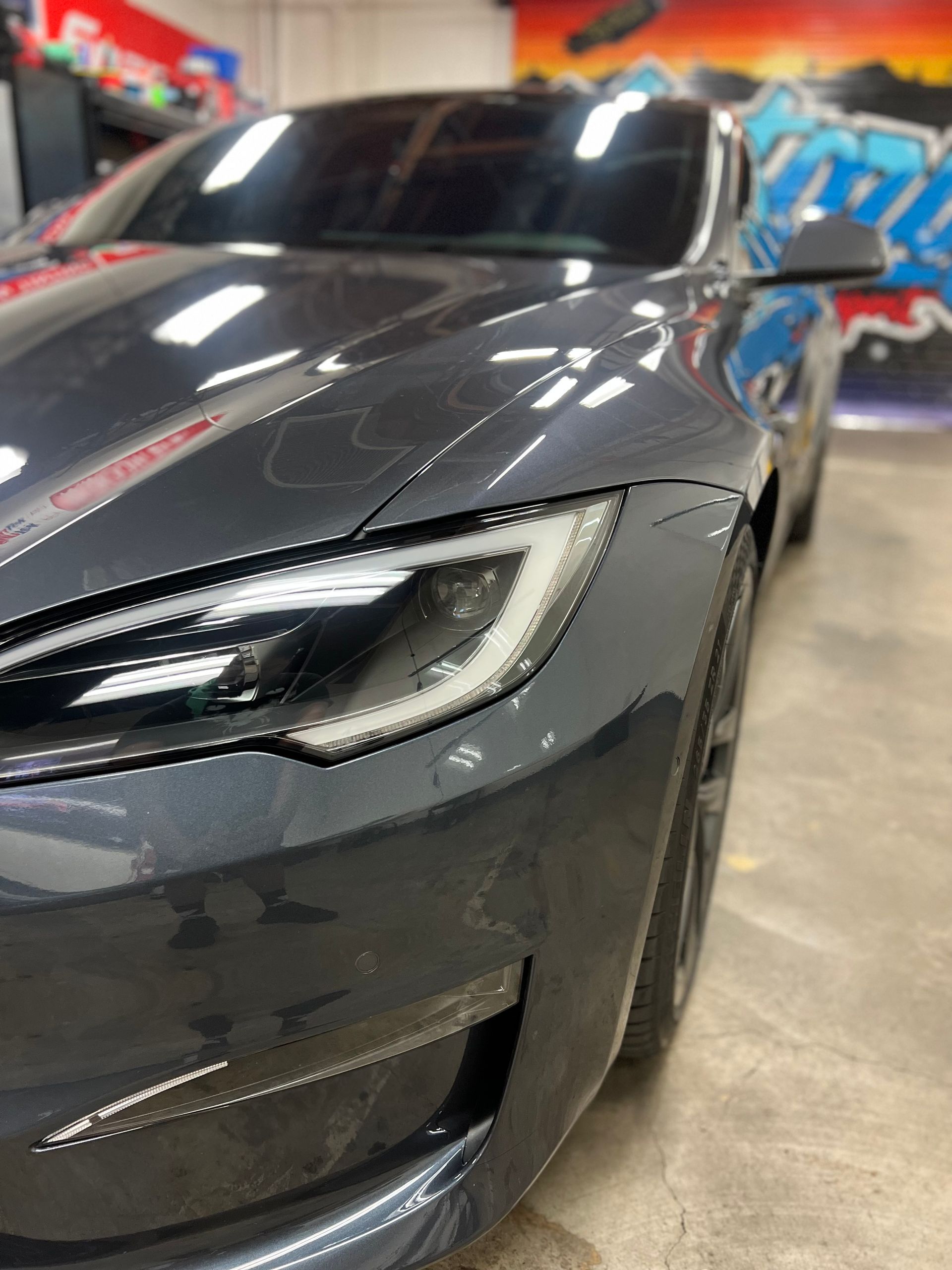 Dark gray sports car front in a garage, close-up of the headlight and hood.
