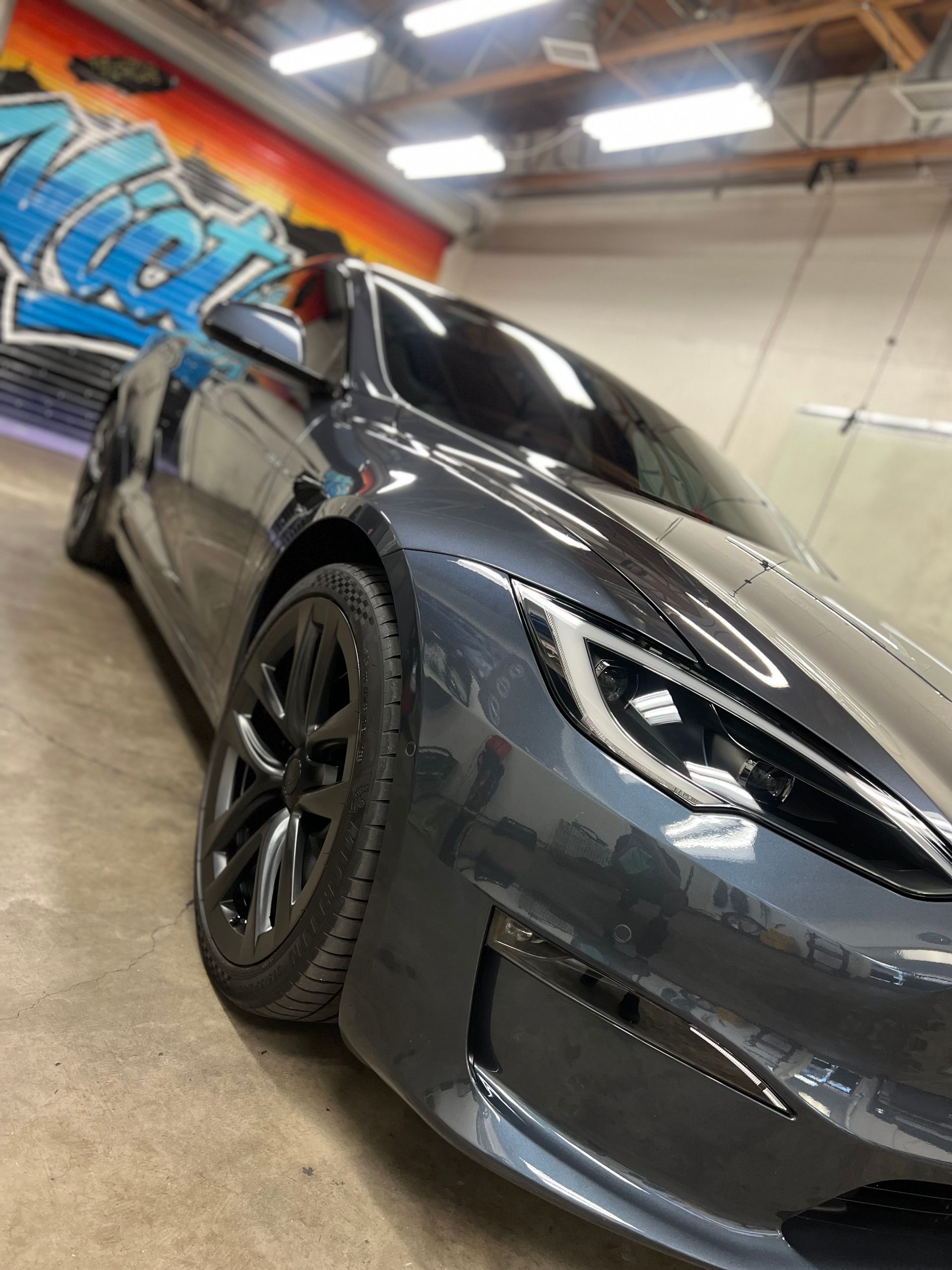 Black sports car in a garage, angled view with graffiti wall in the background
