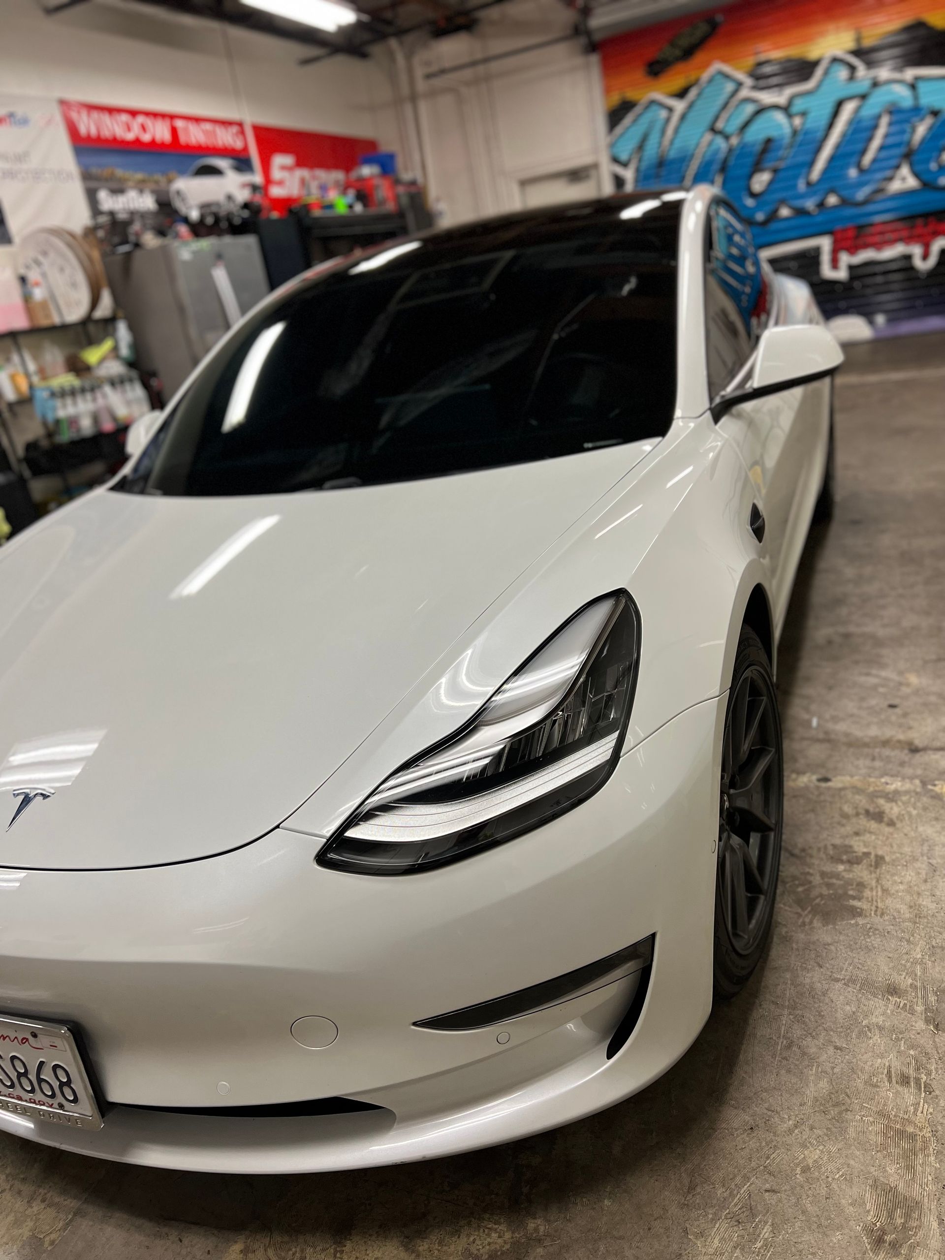 White Tesla sedan in an indoor garage with colorful wall graffiti, front three-quarter view