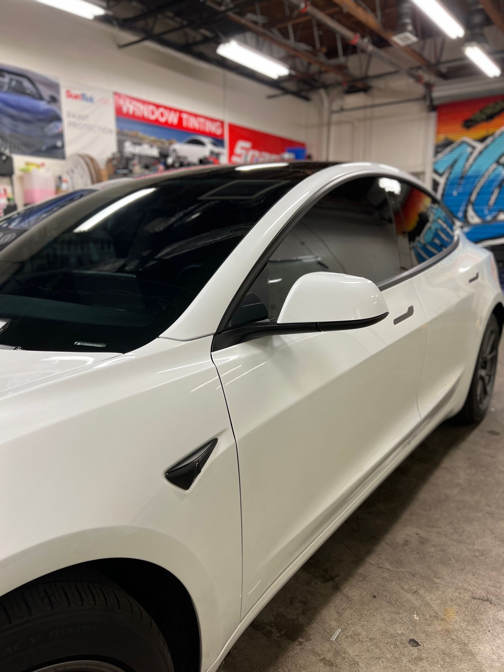 White Tesla parked indoors at a car showroom, side view with tinted windows.