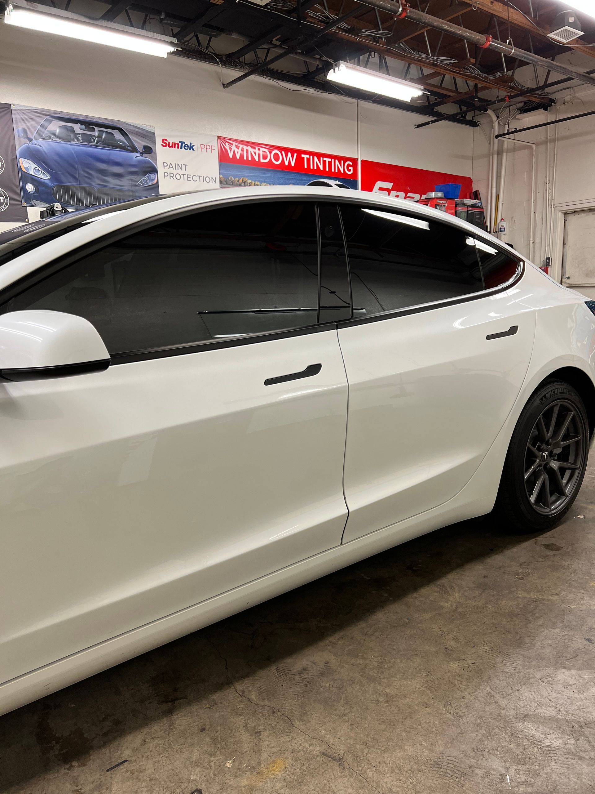 White sedan parked indoors in a garage with tinted windows and black wheels