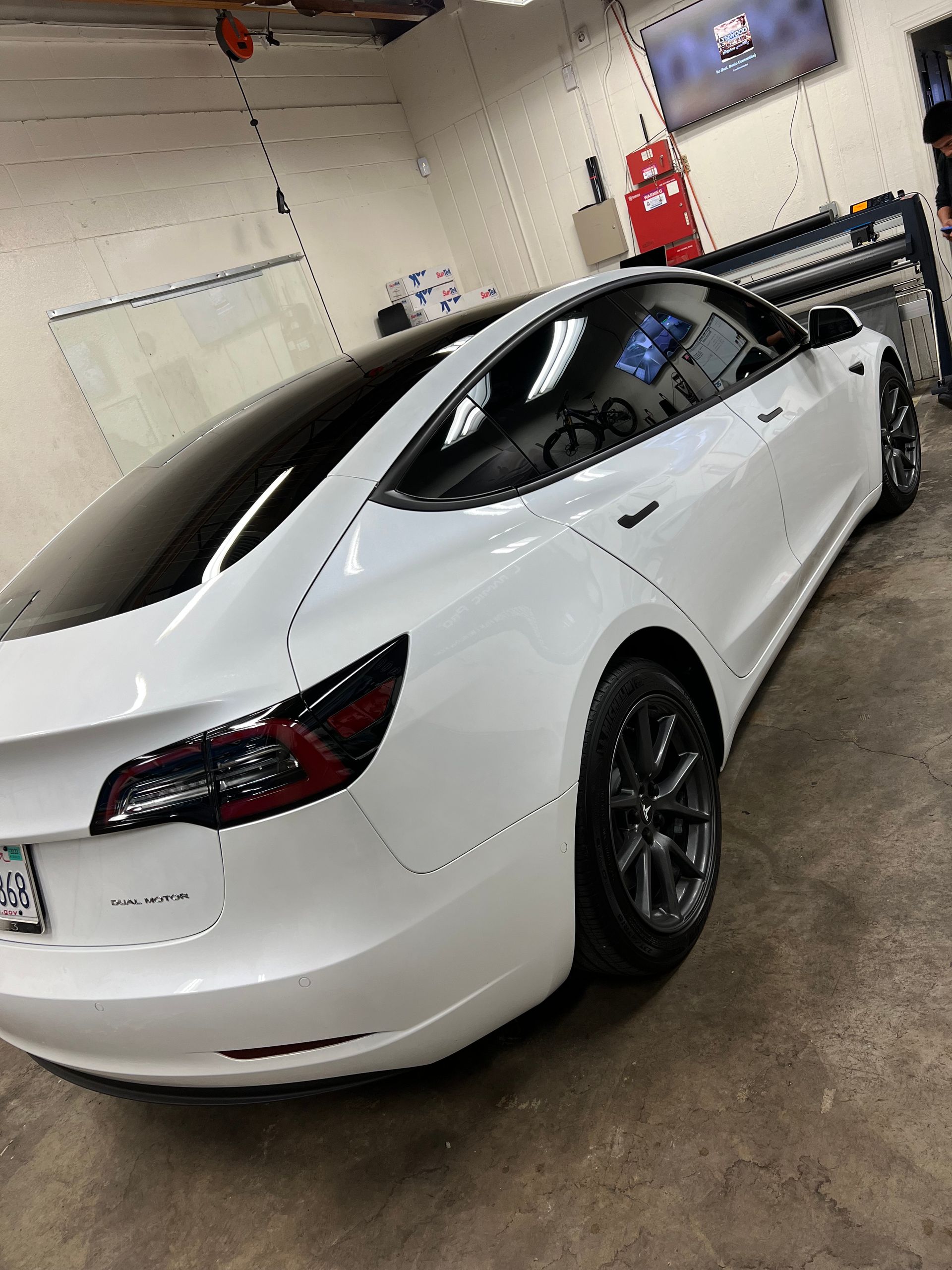 White Tesla sedan in a workshop garage, rear three-quarter view on a concrete floor.