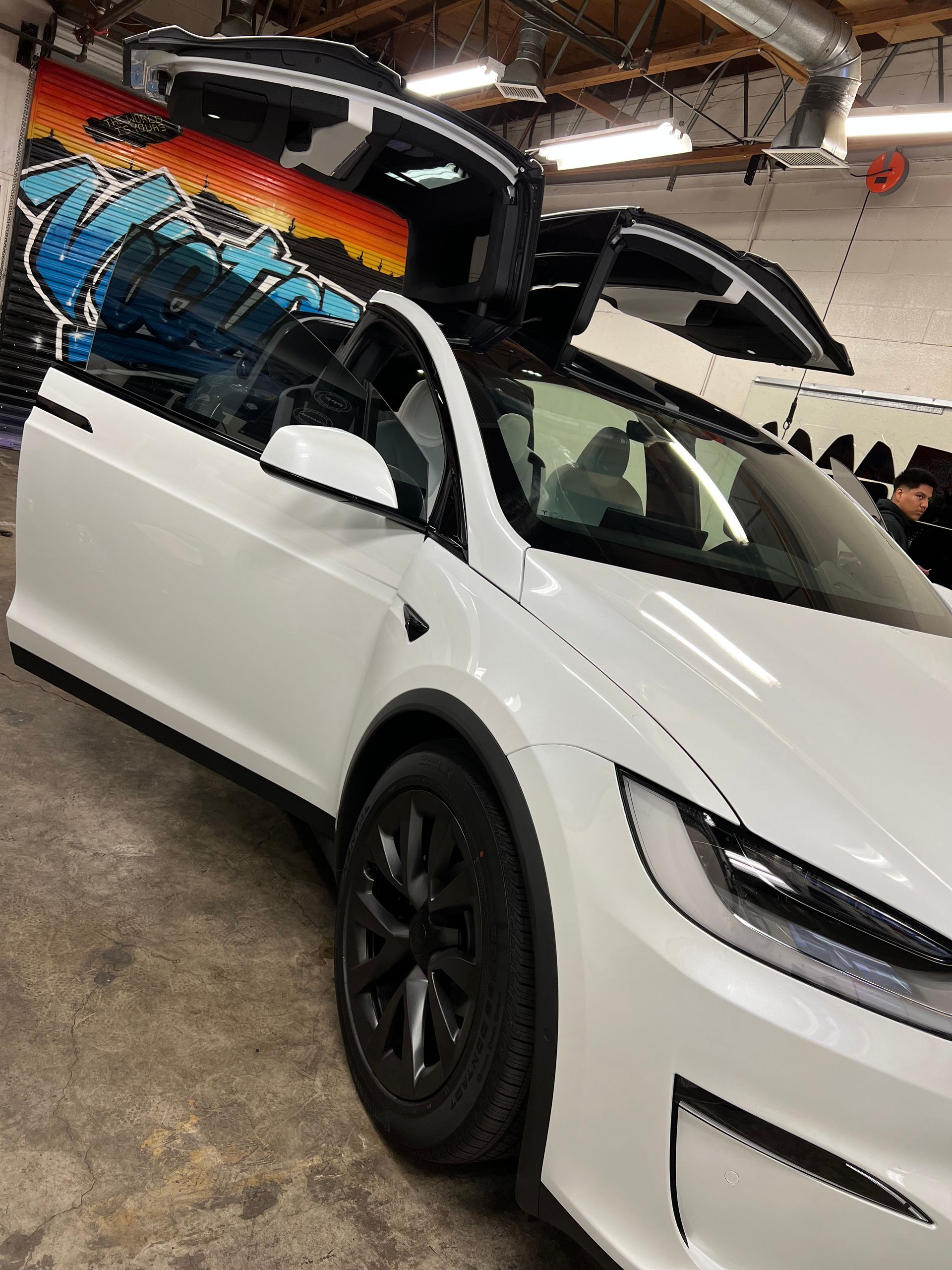 White Tesla with black wheels and colorful roof wrap in an indoor showroom