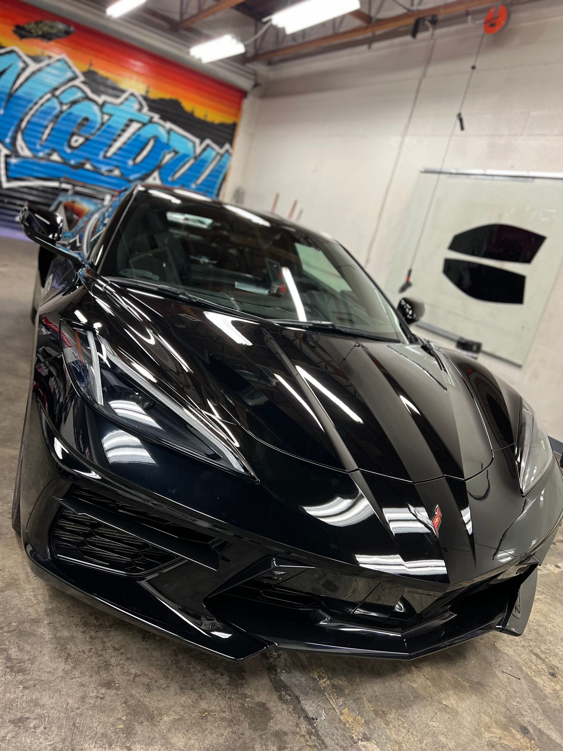 Black sports car in an auto shop, front view with glossy finish and wall mural in the background