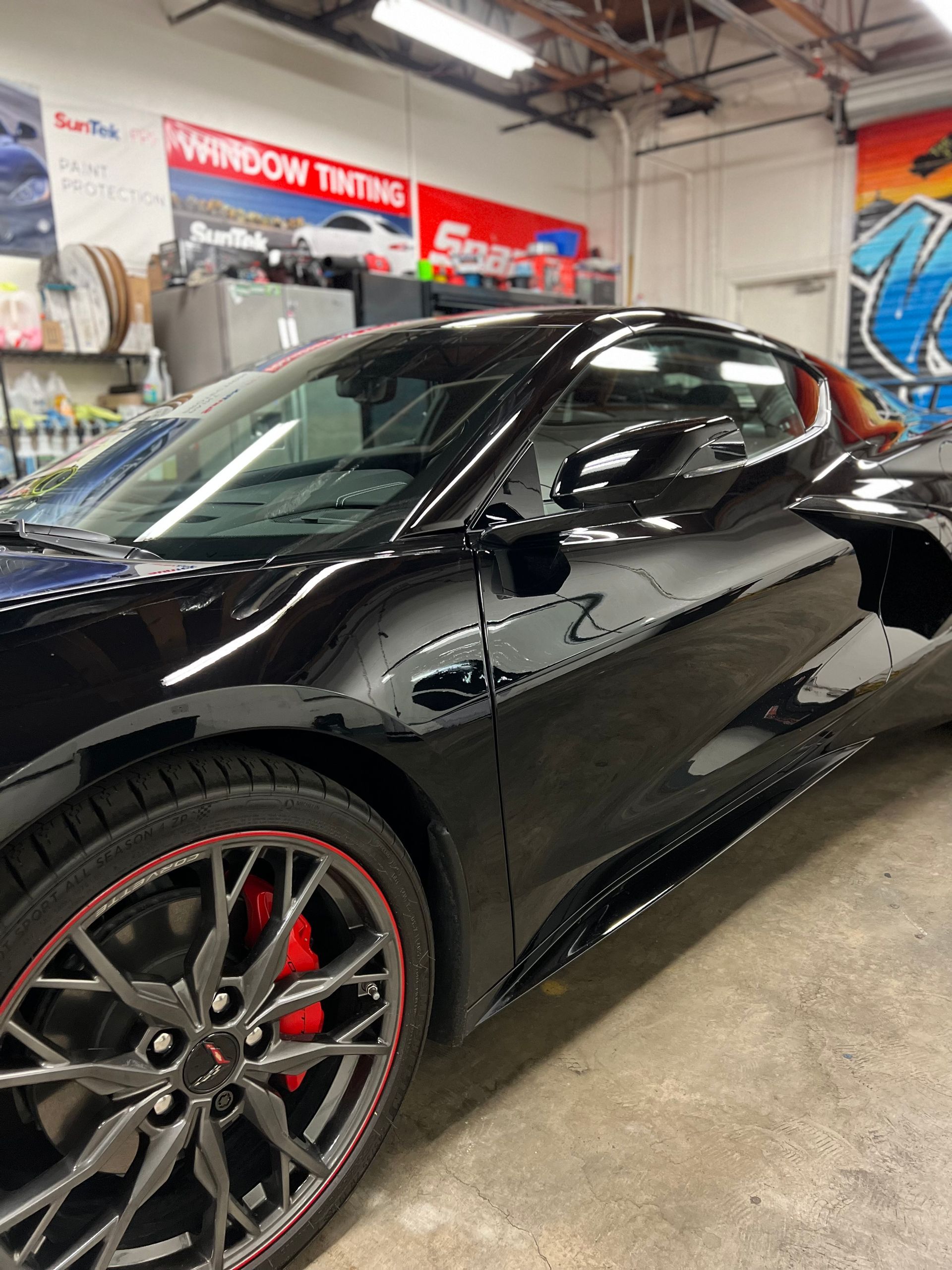 Black sports car in an auto shop, shown from the front side with red brake calipers and glossy paint.