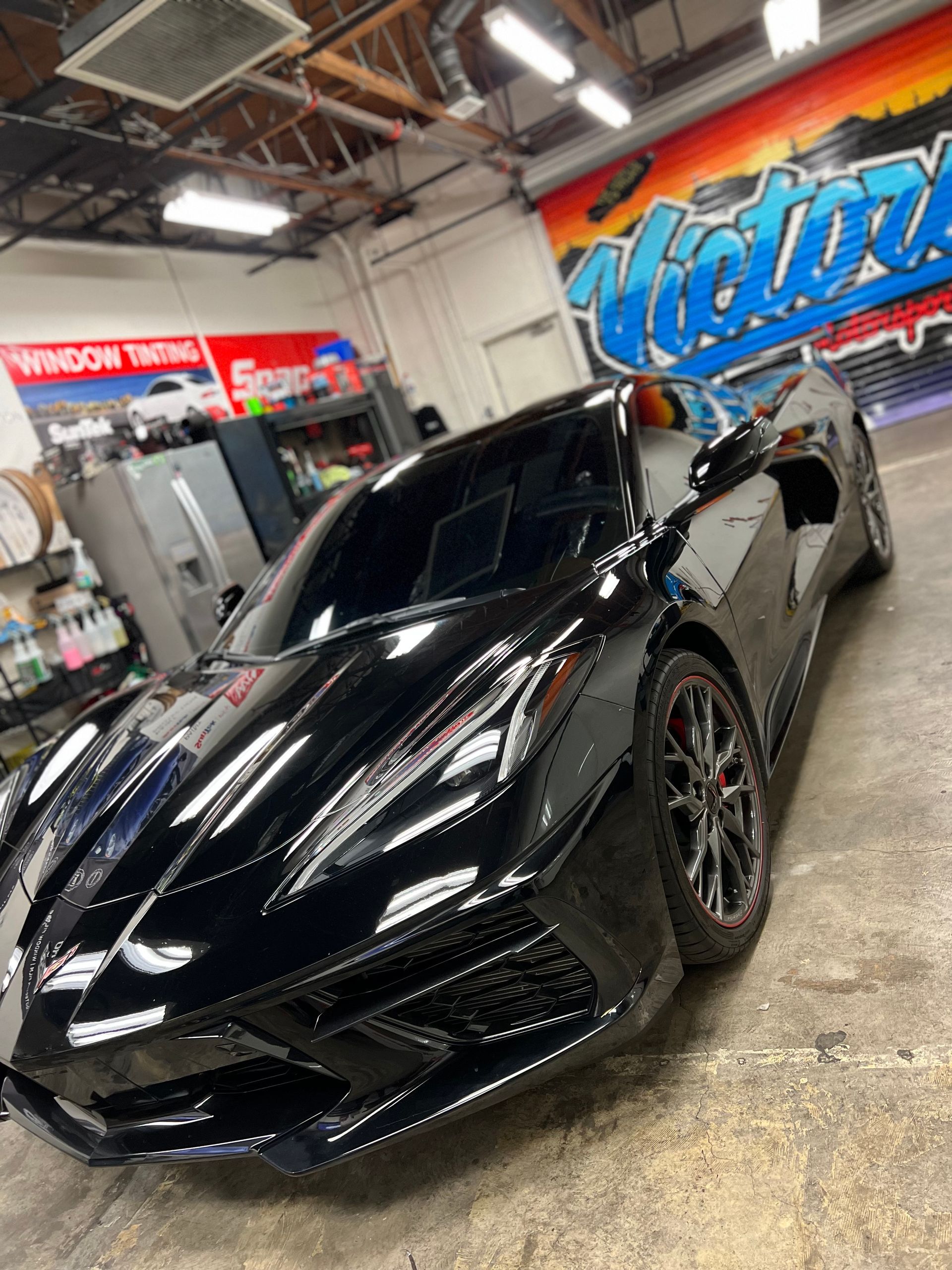 Black sports car in a garage with a colorful mural on the wall