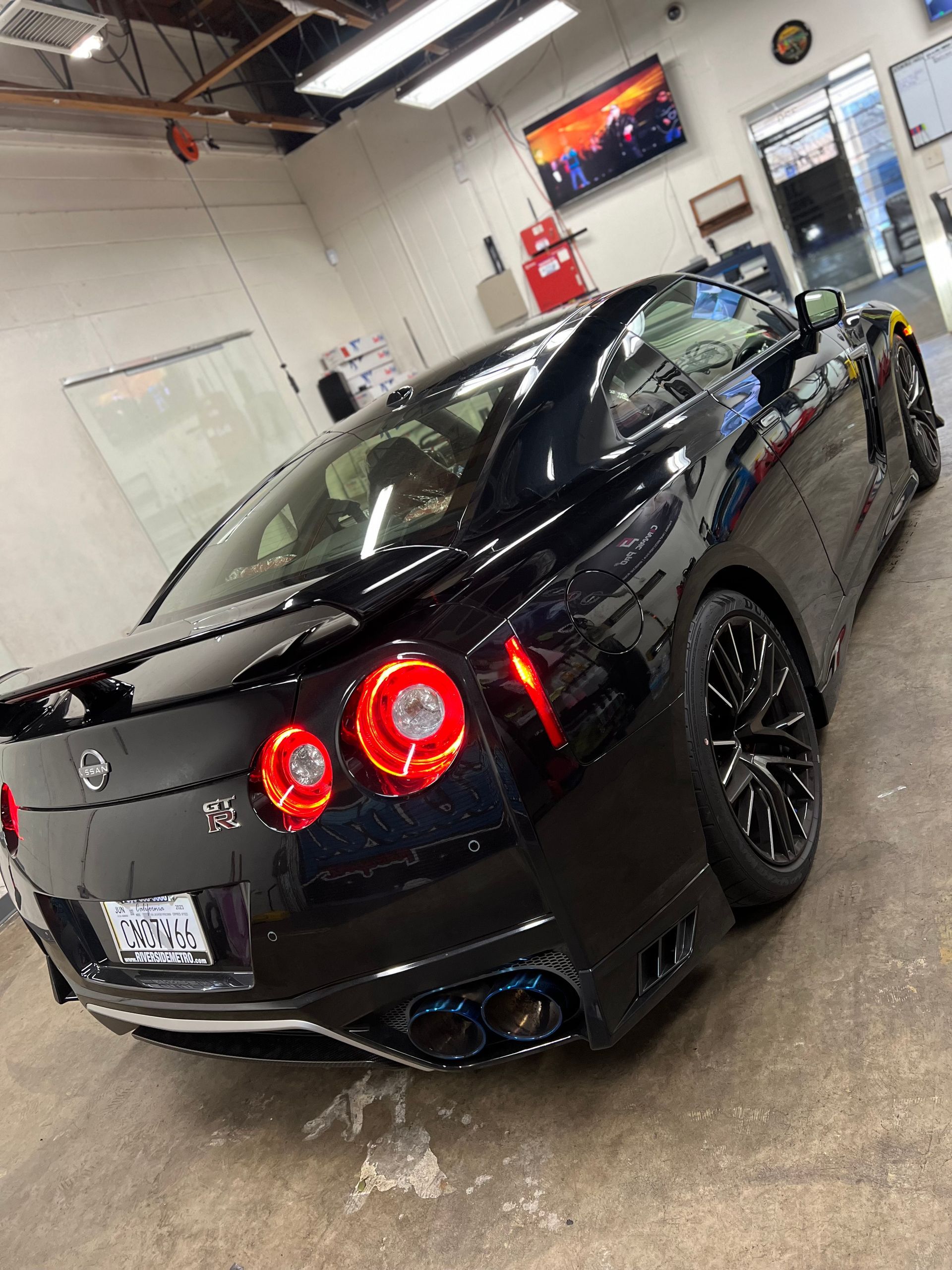 Black sports car in a garage, viewed from the rear with red taillights glowing.