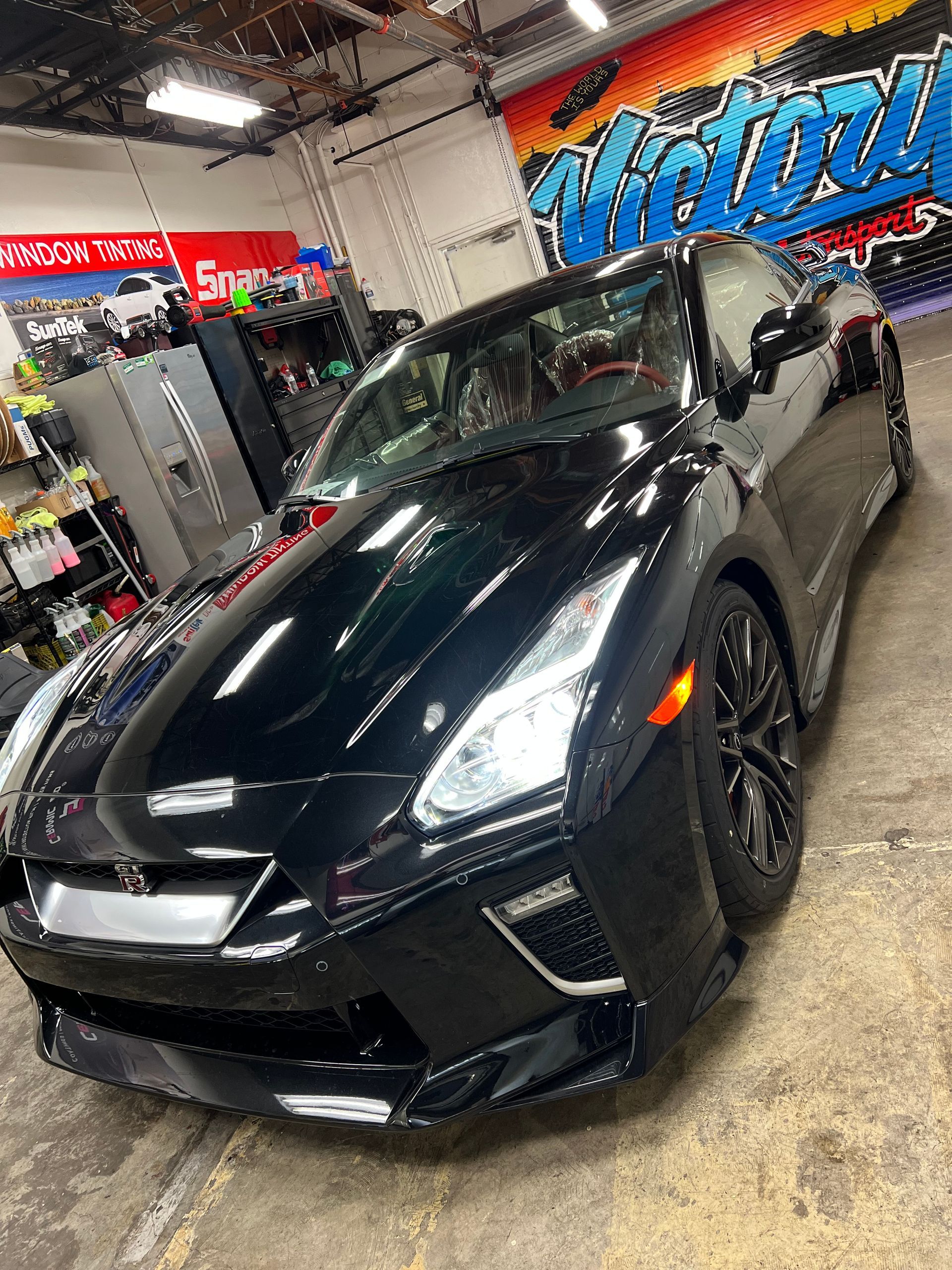 Black sports coupe in an auto shop, angled front view under bright lights