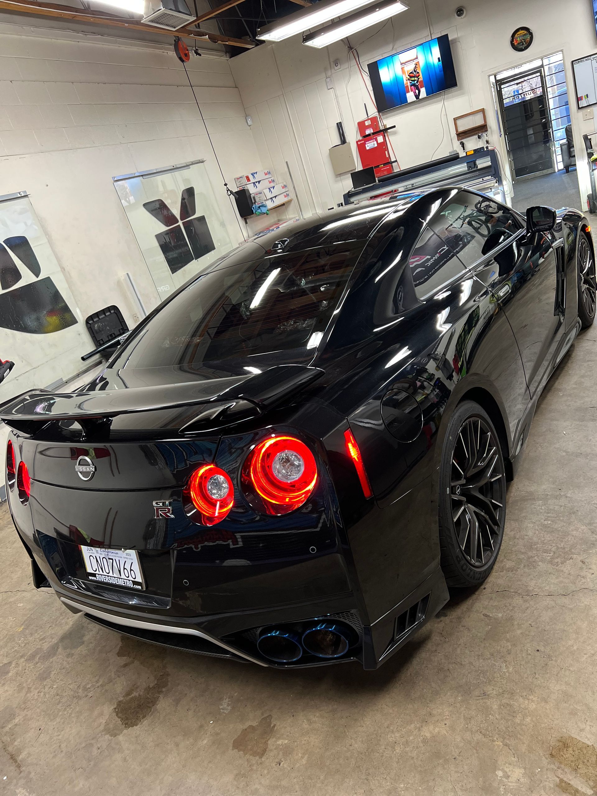 Black sports car parked in a garage, rear view with red taillights and glossy finish