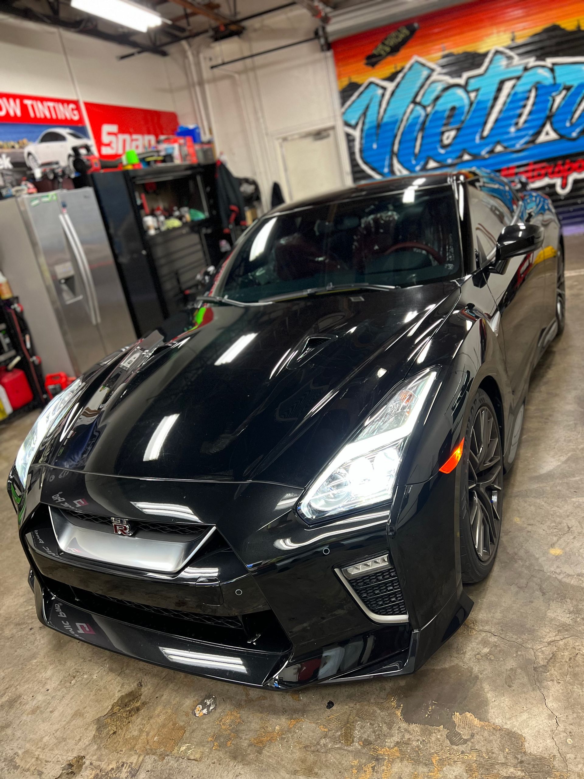 Black sports car in an auto shop, shown from the front-left angle.