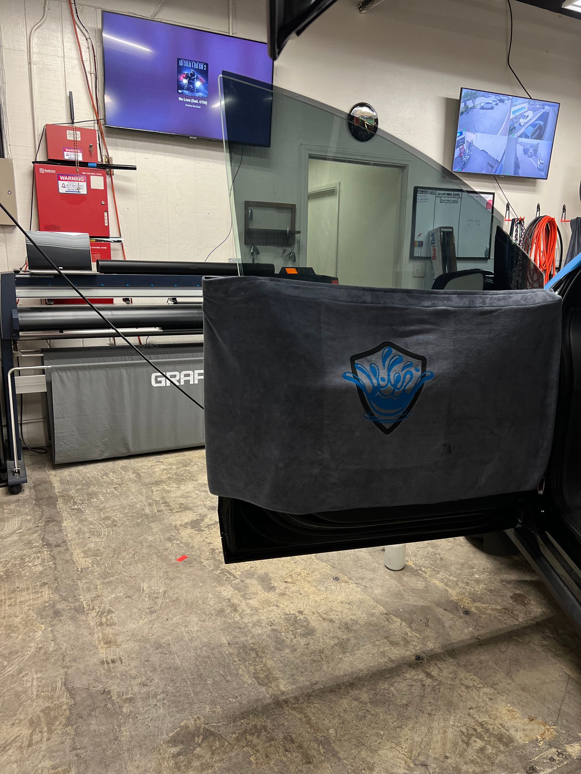 Industrial workshop with a black fabric barrier, blue shields on wall-mounted screens, and machinery in the background