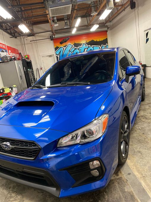 Blue sports sedan in an indoor garage with colorful graffiti on the back wall.