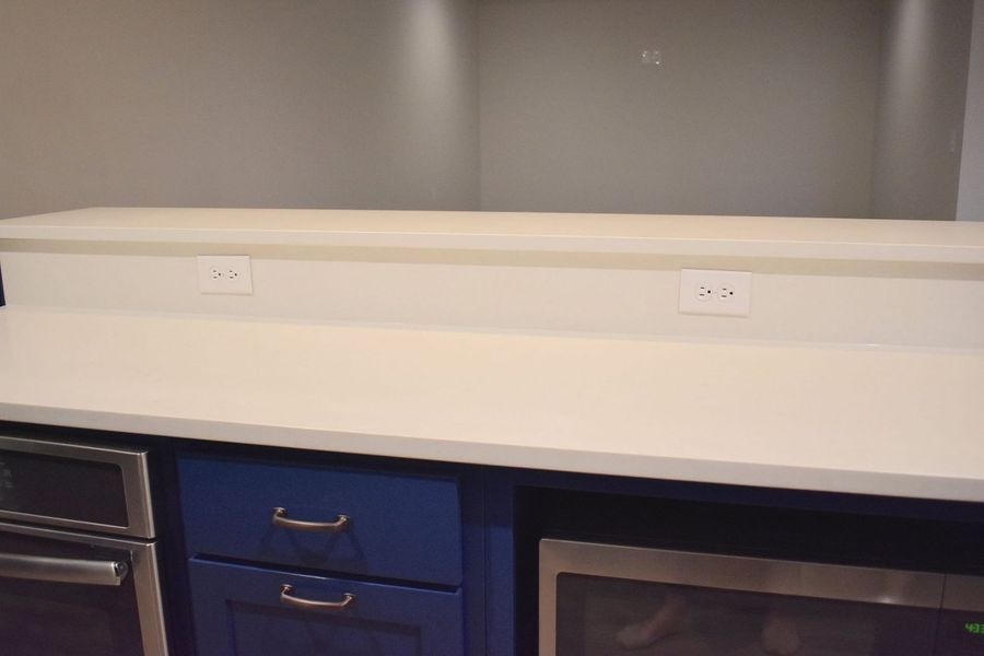 Kitchen counter with white surface, blue cabinets, electrical outlets, and built-in appliances.