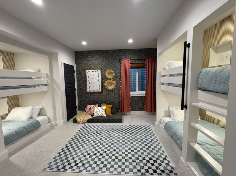 Modern bunk room with four built-in beds. Checkered rug, gray walls, black door, and orange curtains.