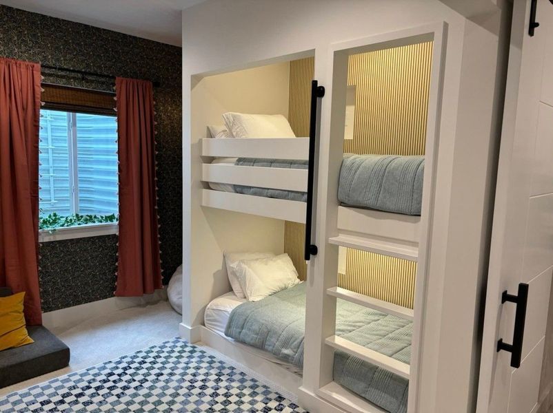 Built-in bunk beds in a room with a window, curtains, and a patterned rug.
