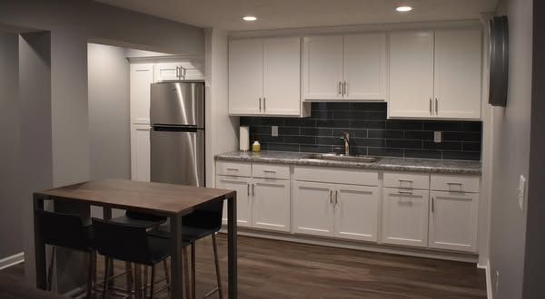 Kitchen with white cabinets, stainless steel appliances, dark backsplash, and a table with stools.