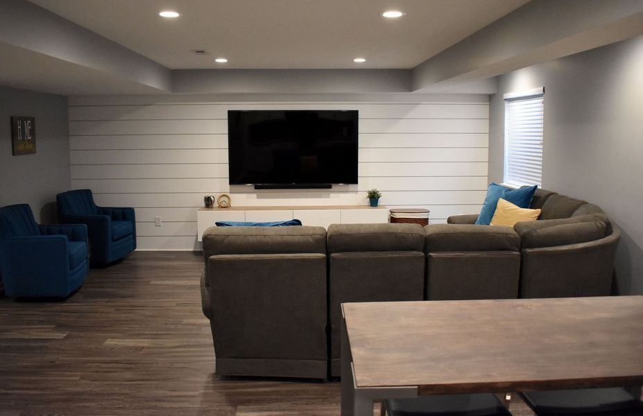 Living room with TV on a shiplap wall, gray sectional sofa, and blue armchairs.