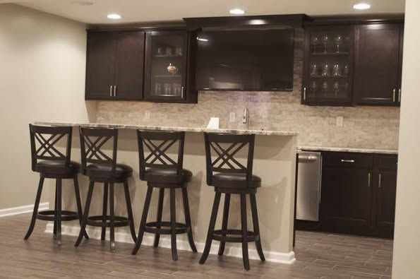 Dark wood bar with bar stools, cabinets, and a television on a light-colored wall.