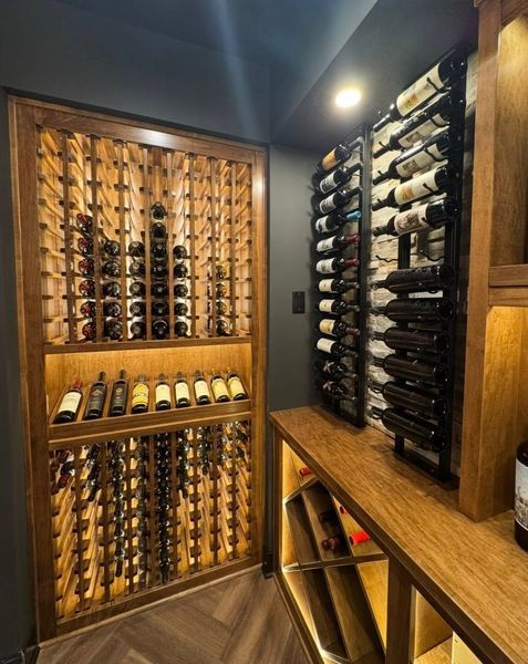 Wine cellar with wooden racks, holding numerous bottles. Warm lighting illuminates the space, creating a luxurious feel.