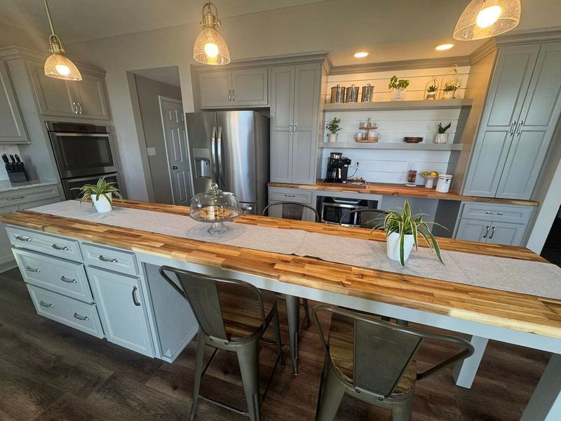 Kitchen island with wooden countertop, grey cabinets, and pendant lights.