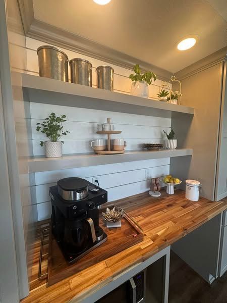 Coffee station with a coffee maker, wooden countertop, shelves, and various containers and plants.