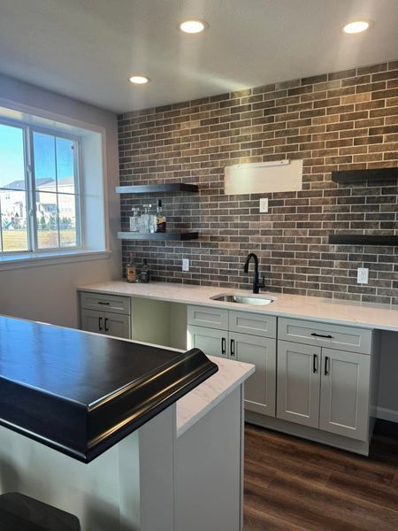 Basement bar with brick wall, floating shelves, white countertops, and gray cabinets.